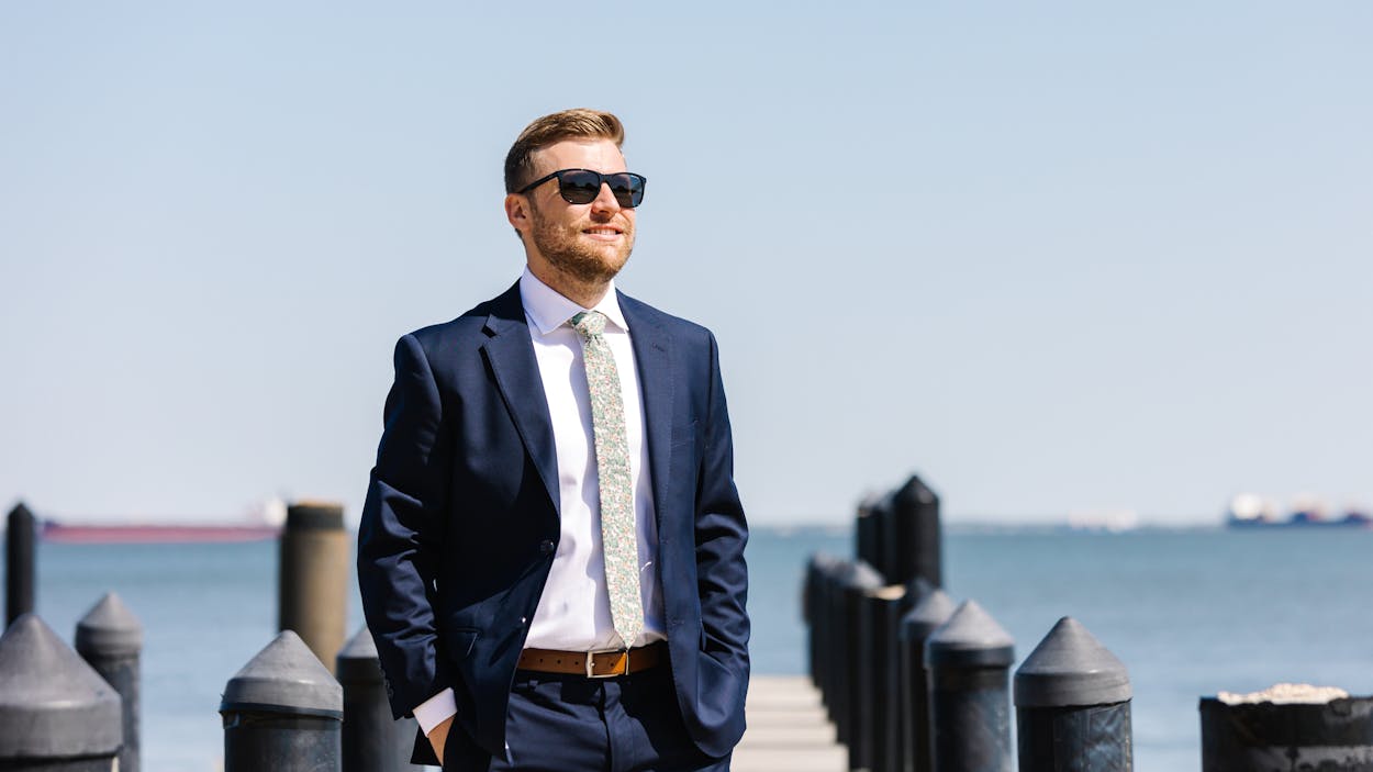Wedding guest wearing navy blue suit for beach wedding with green patterned tie standing by ocean