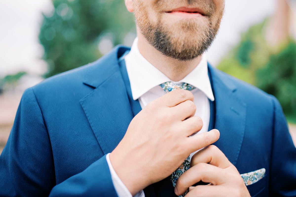 Man wearing blue suit and adjusting patterned tie for wedding guest attire