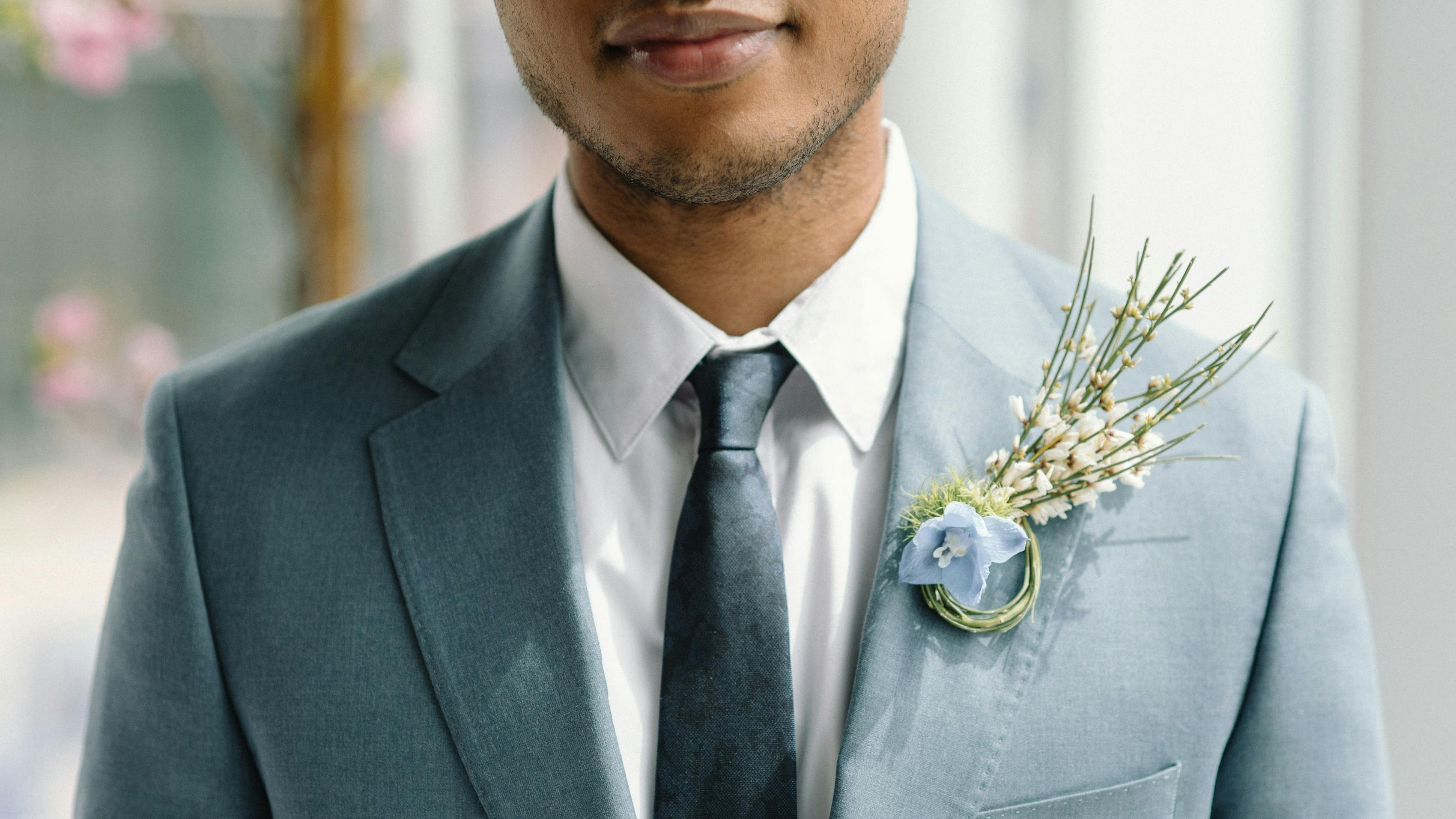Classic tie knot demonstrated with a black brocade silk slim tie to match his light grey suit