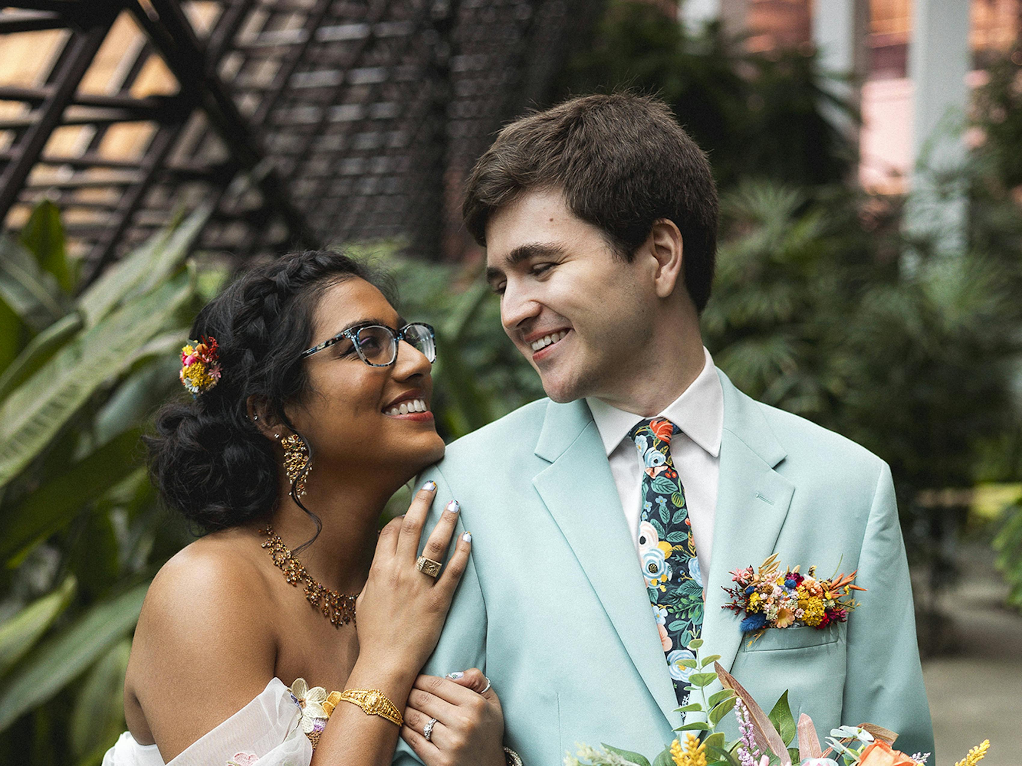 Bride wears floral dress to colorful wedding while groom looks lovingly in a seaglass suit for men