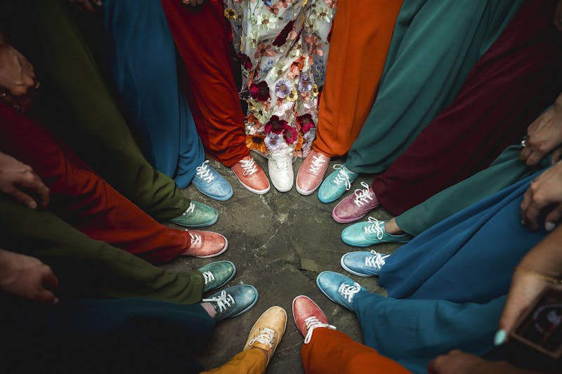 Bridesmaids gathered in a circle wearing various shades of hand-dyed Keds to create a color coordinated wedding sneaker look.