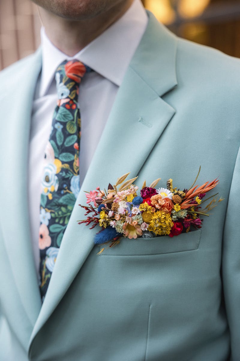 Groom in a seaglass suit for men, styled with a dried floral pocket boutonniere and bold floral tie