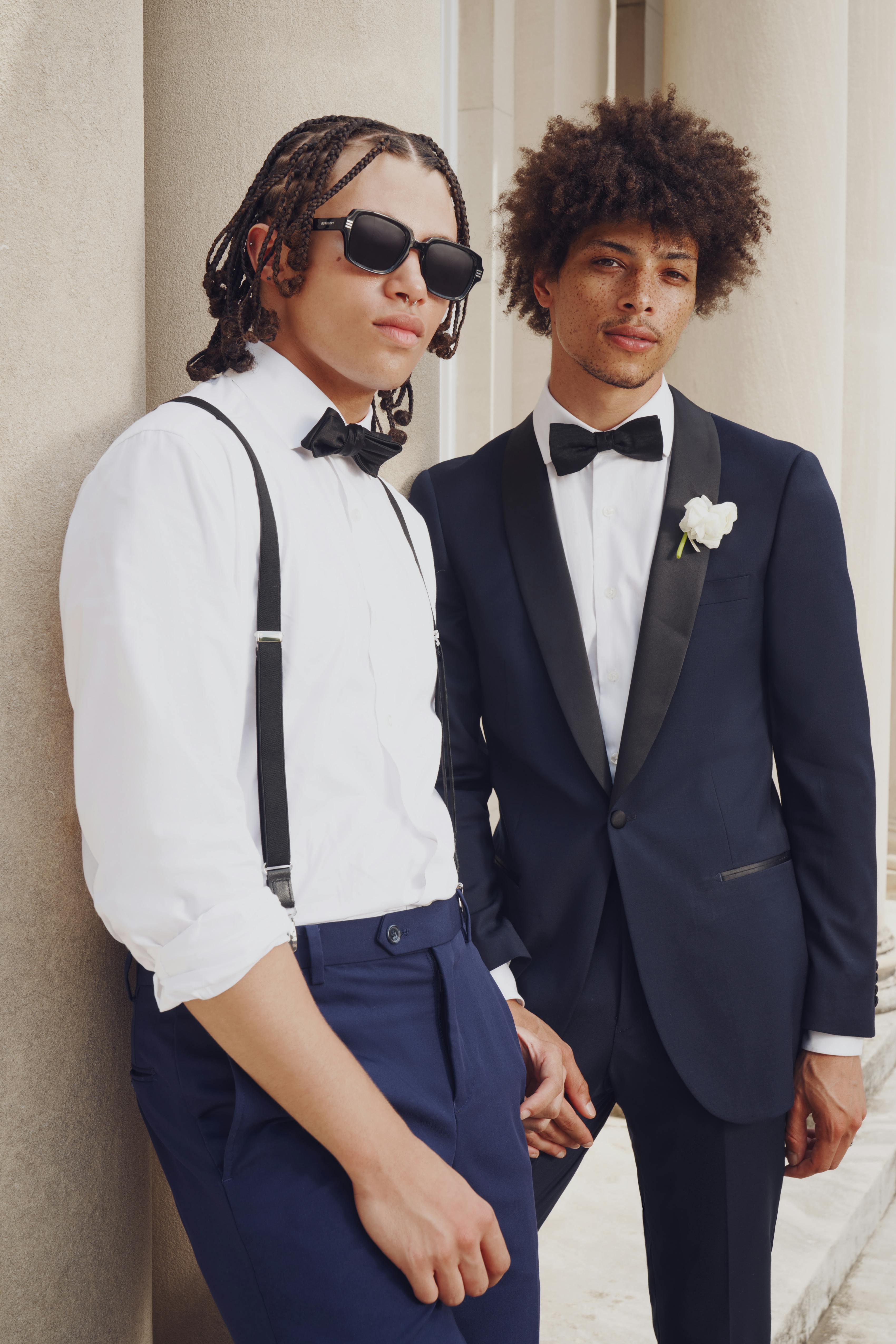 Groomsman wearing blue suit with suspenders and groom wearing navy blue tuxedo for wedding