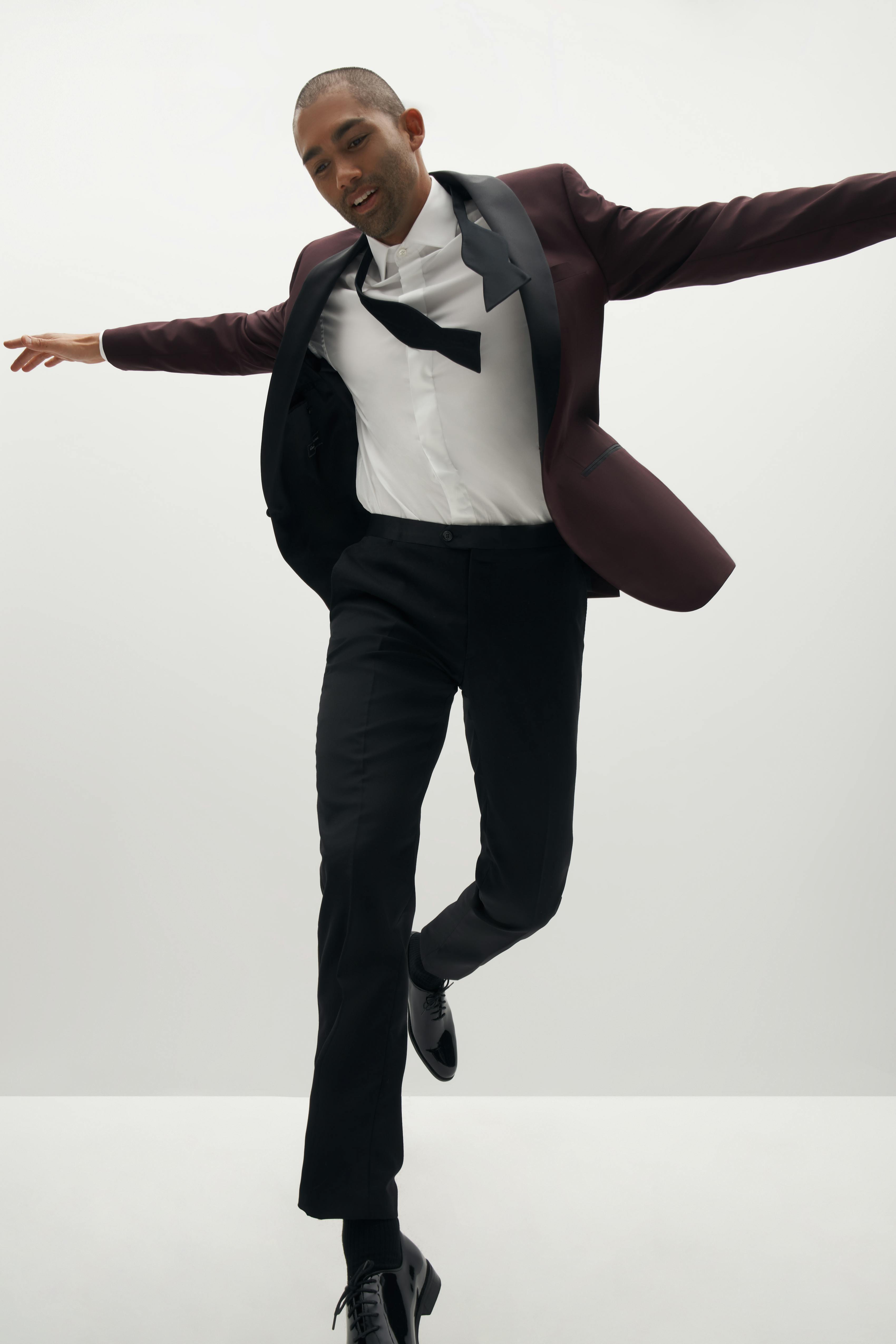 Man dancing while getting ready for black tie wedding in burgundy tuxedo