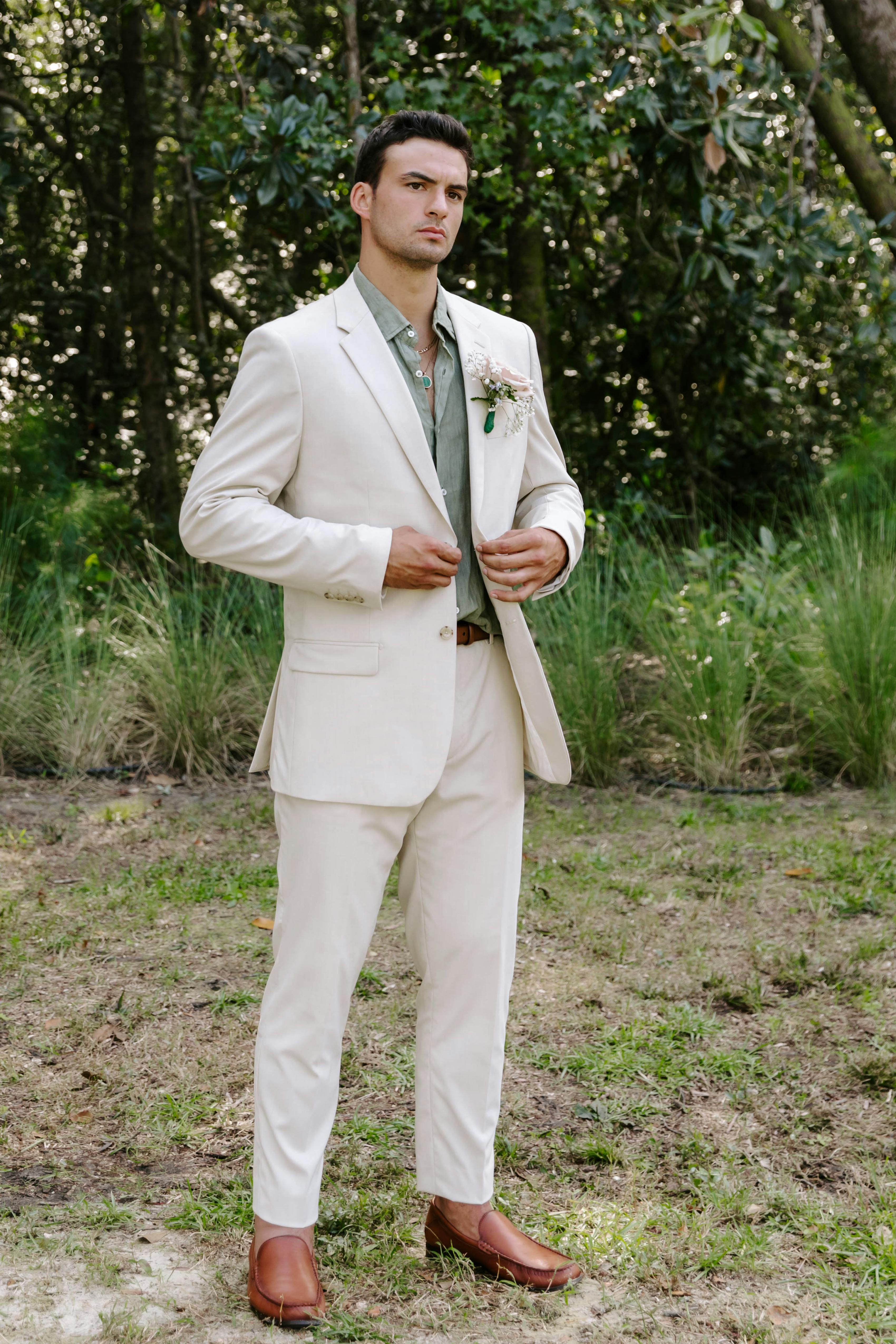 Casual summer wedding attire for men with tan suit and sage green dress shirt at outdoor wedding