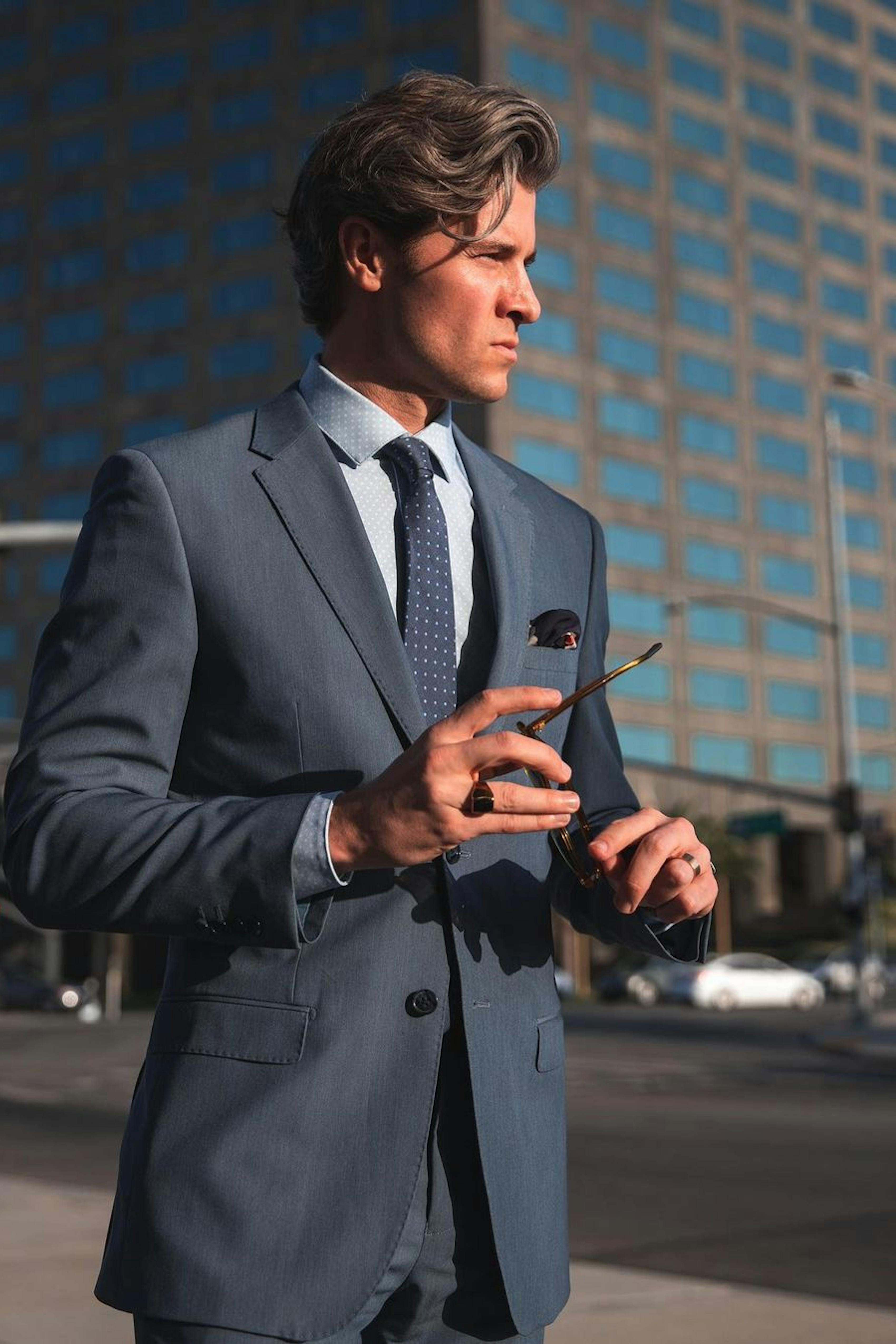 Cool men's summer wedding guest outfit for semi-formal dress code with light blue suit and blue accessories.