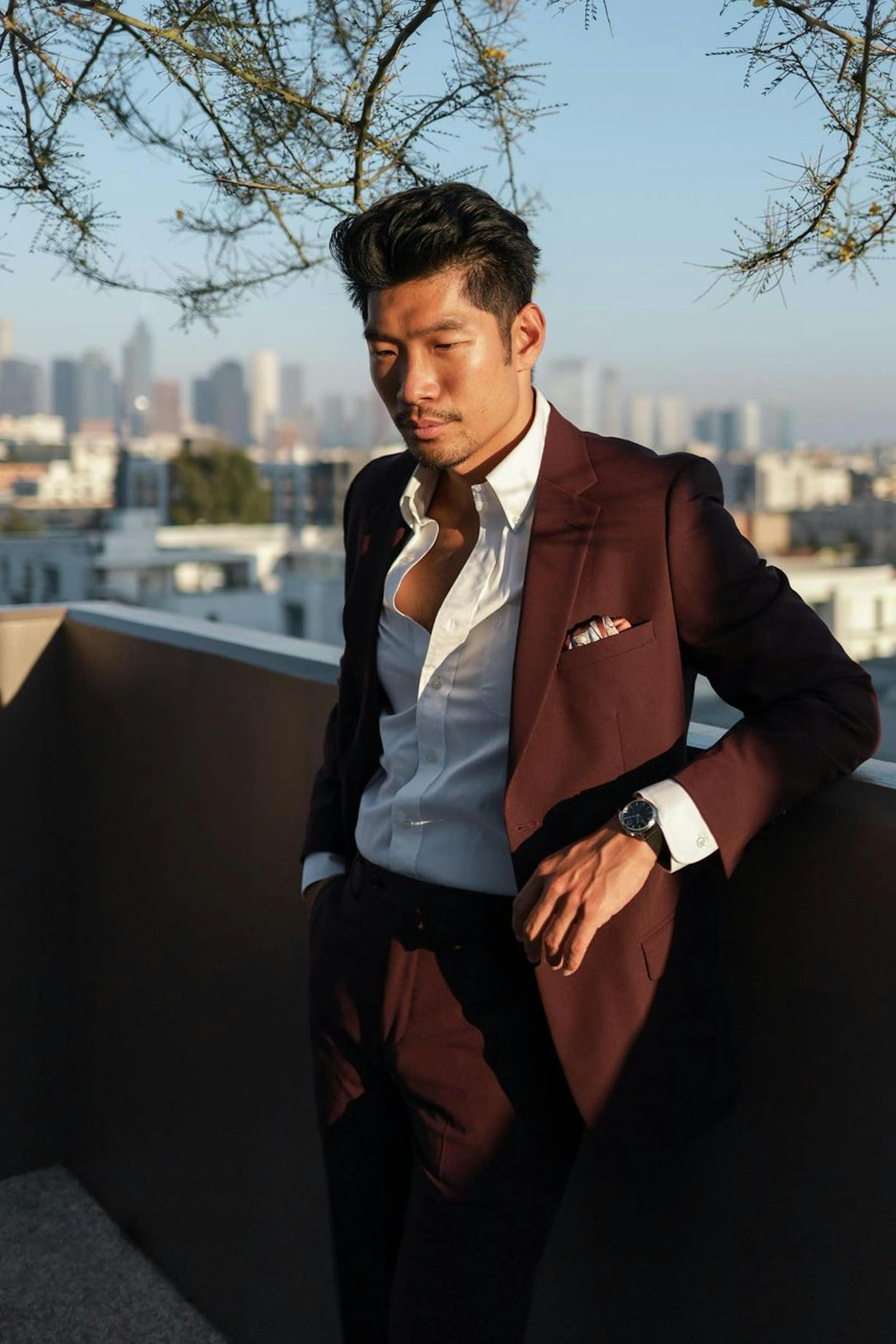 Man wearing formal dress code summer wedding outfit in burgundy suit with silk pocket square on city rooftop