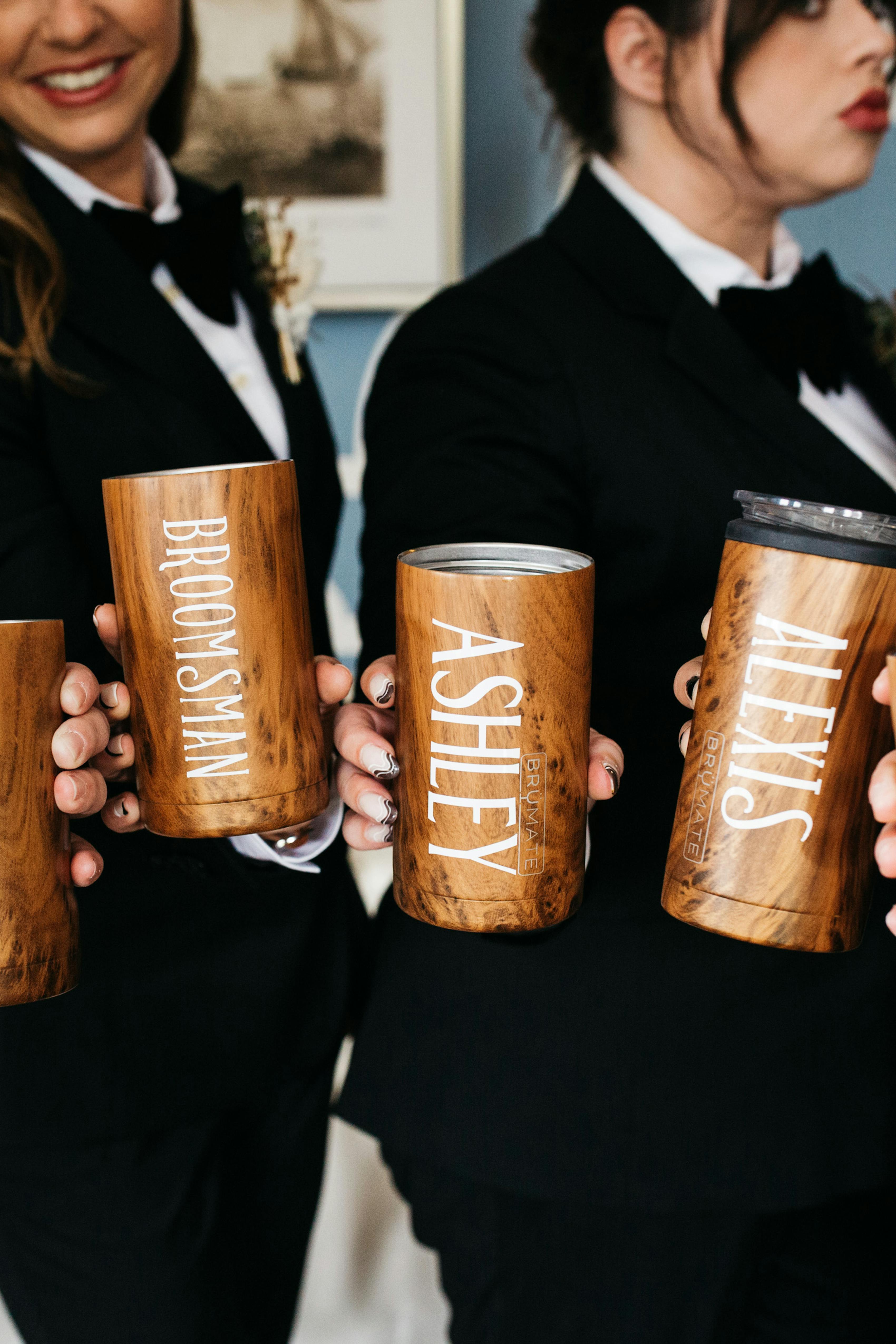 Women wearing tuxedos holding personalized insulated tumblers for groomsmaids and groomsmen gifts.