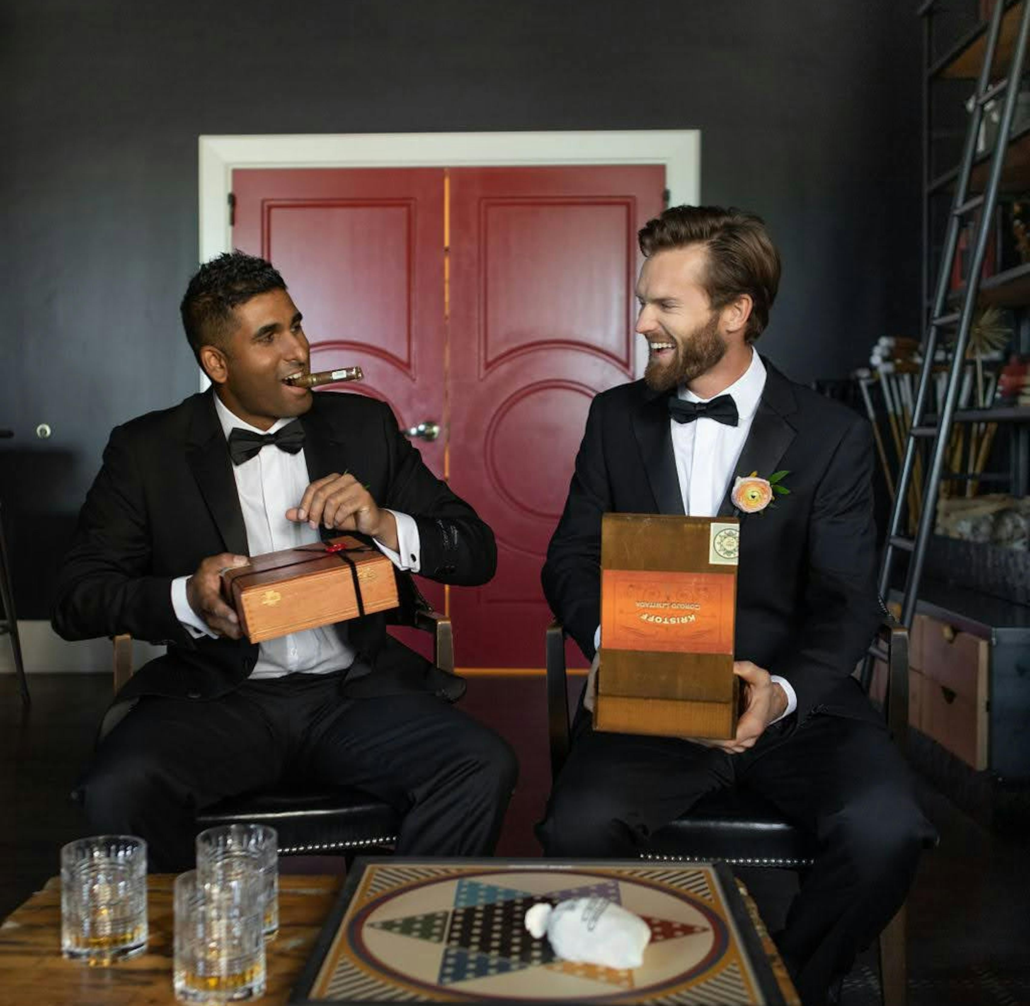 Groomsmen wearing black tuxedos opening their wedding party gift cigar boxes