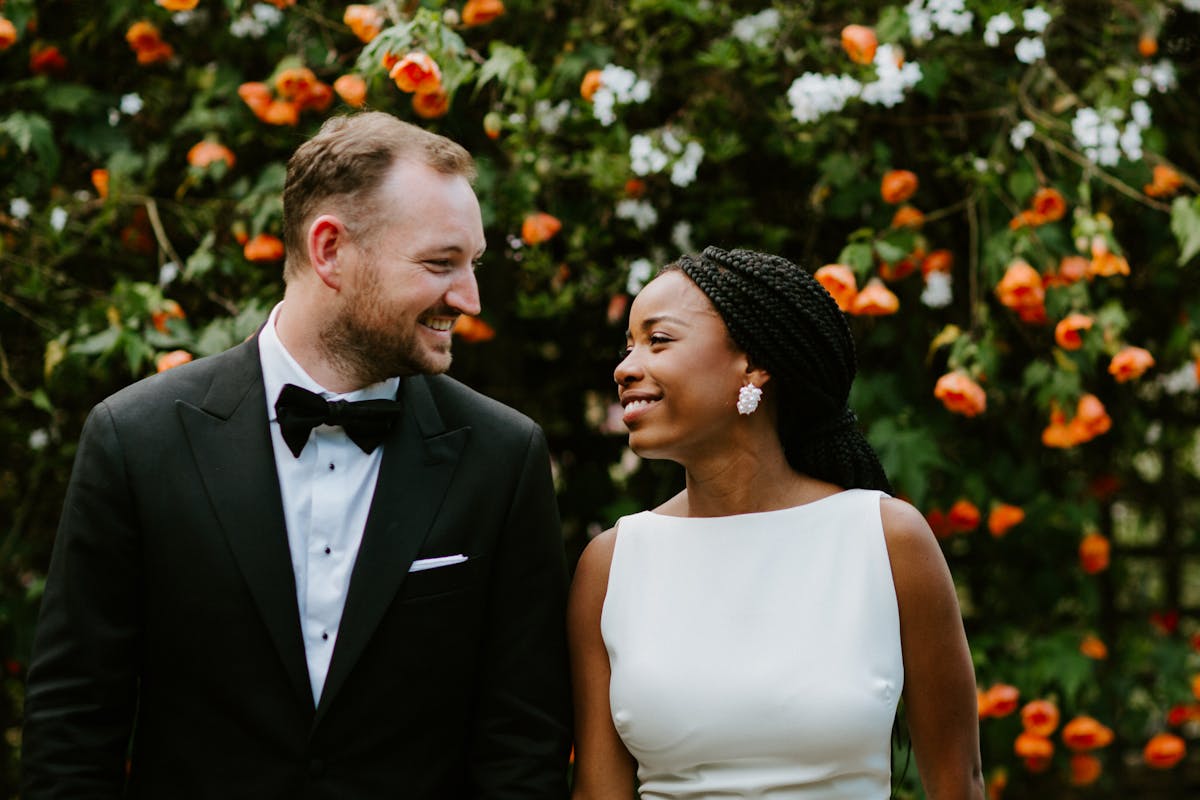 Black tie garden wedding bride and groom smiling in front of rose wall