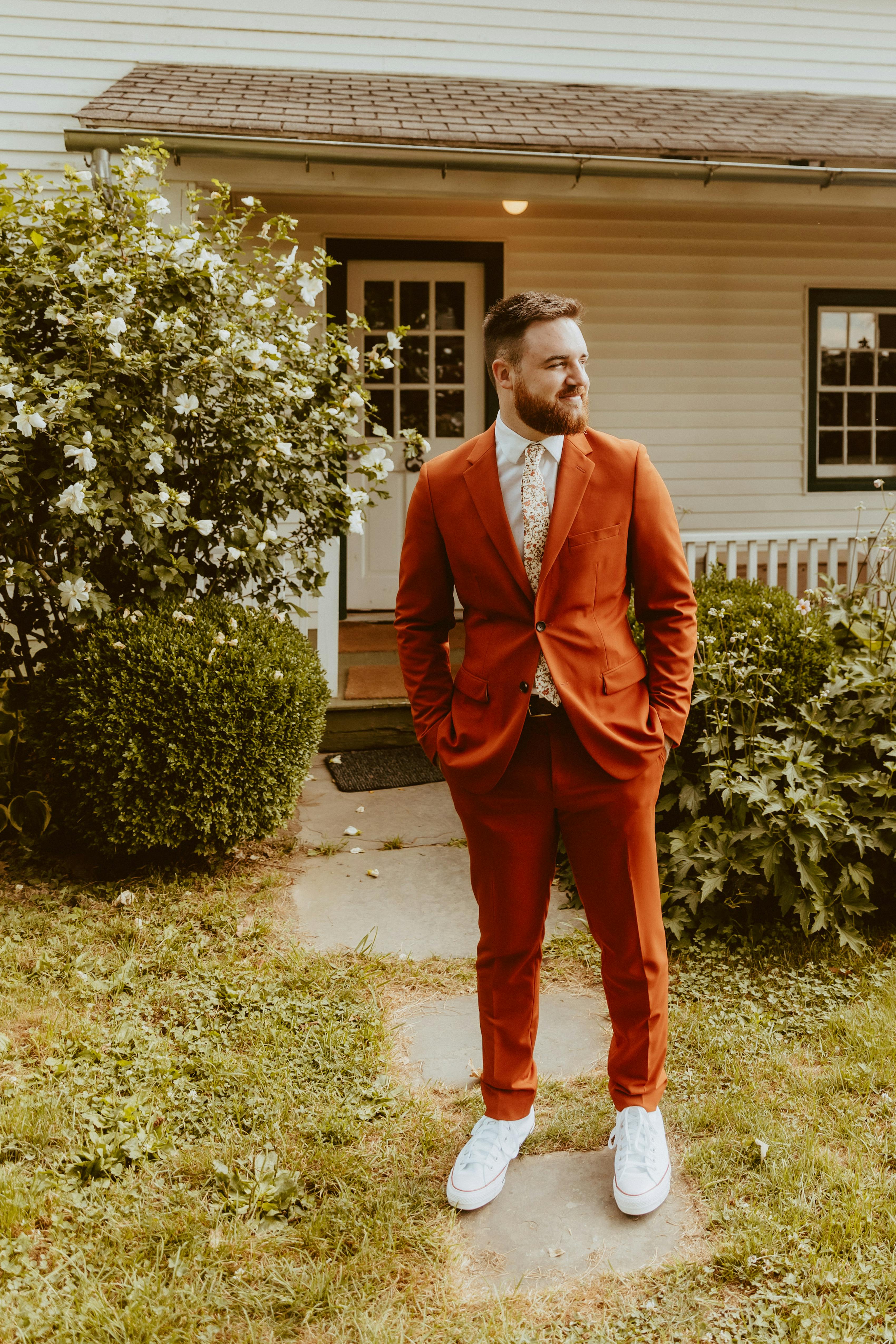 Men's fall casual wedding suit in rust orange with white sneakers and no tie.