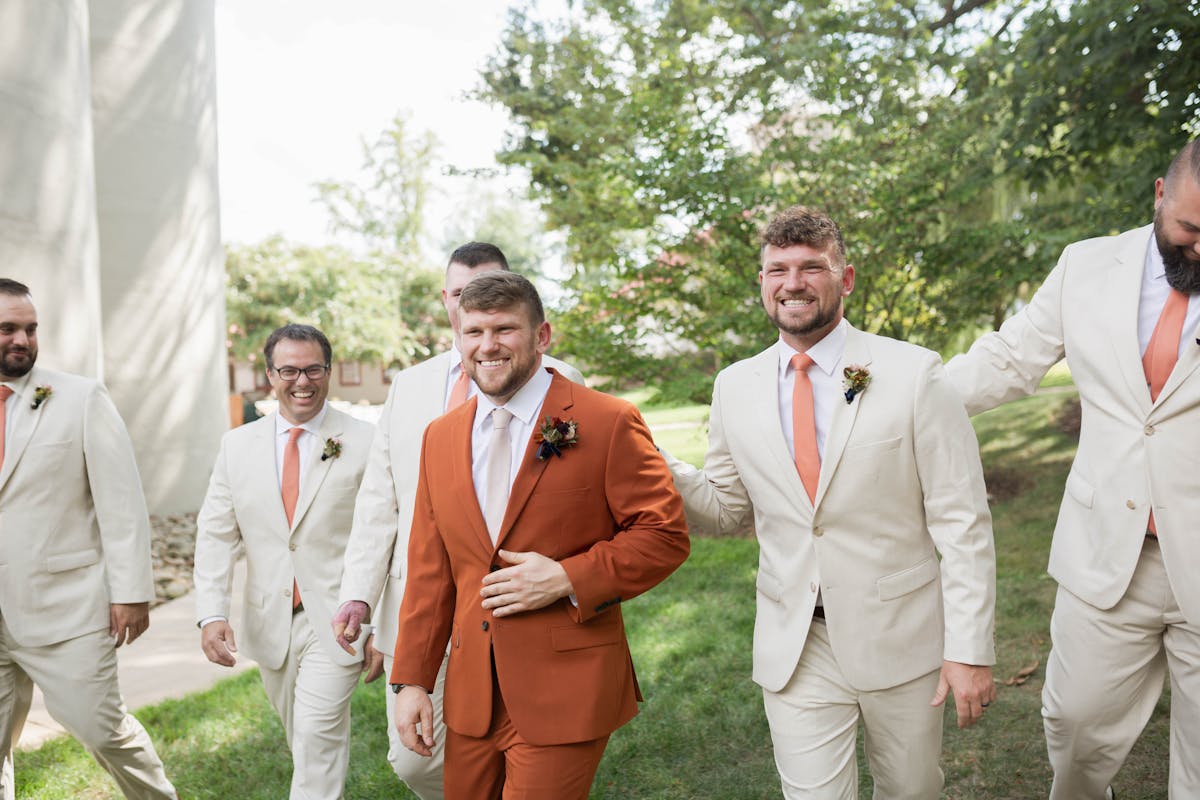 Earth tone wedding party attire with groom wearing rust orange suit and groomsmen in tan suits.