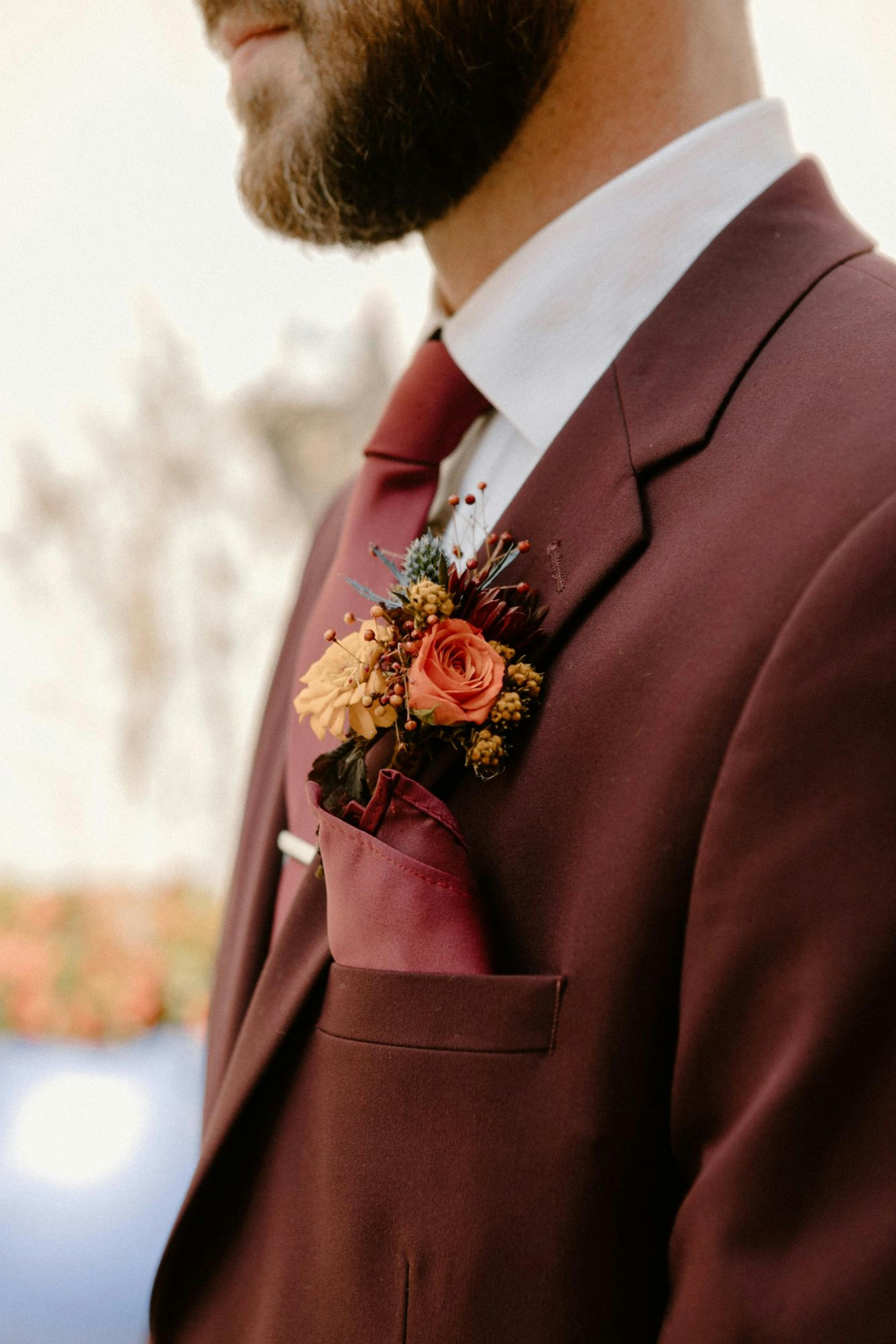 Groom wearing red wedding suit with burgundy suit tie and boutonnière.