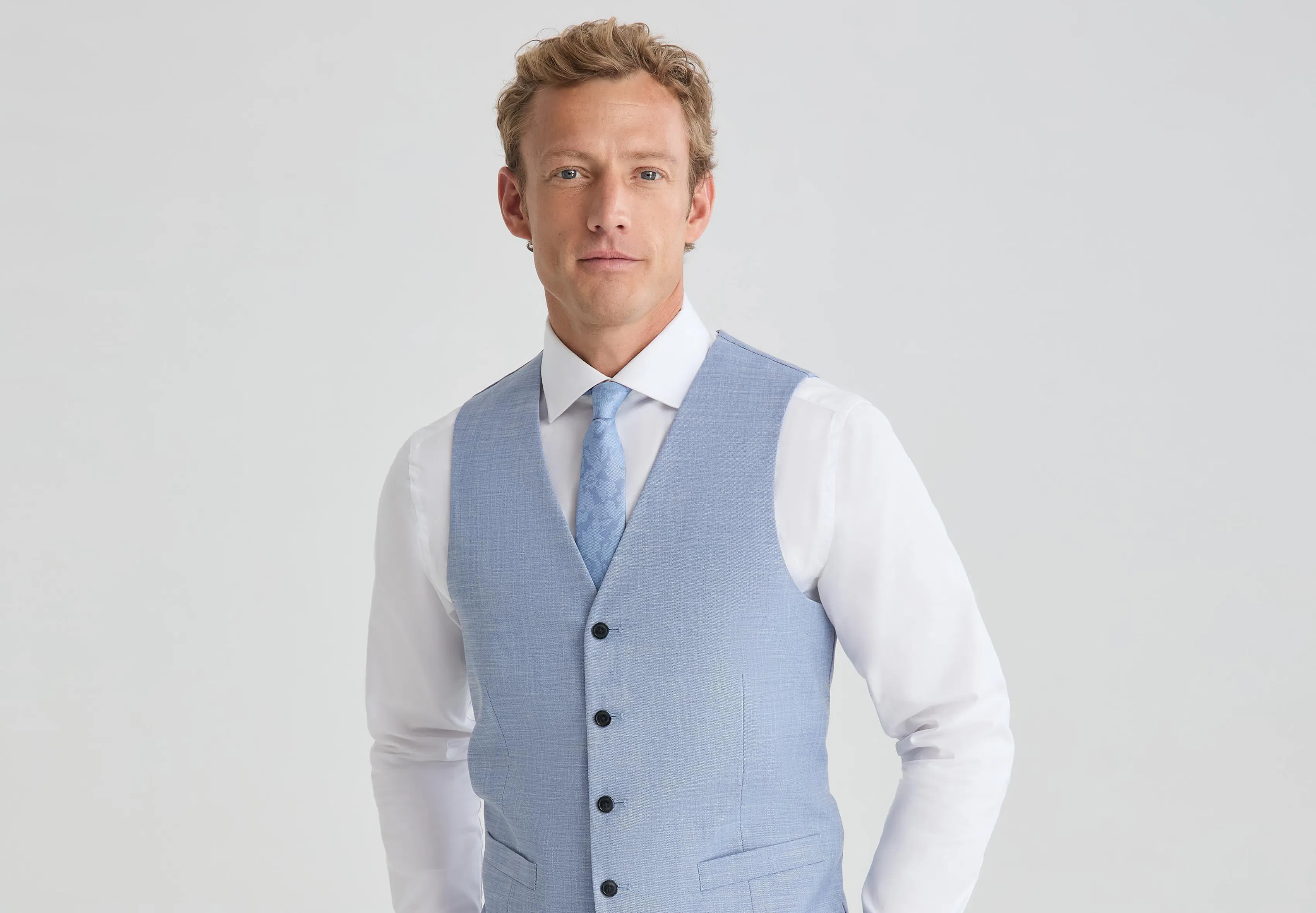 Man wearing a light blue vest with a white dress shirt and matching blue tie.