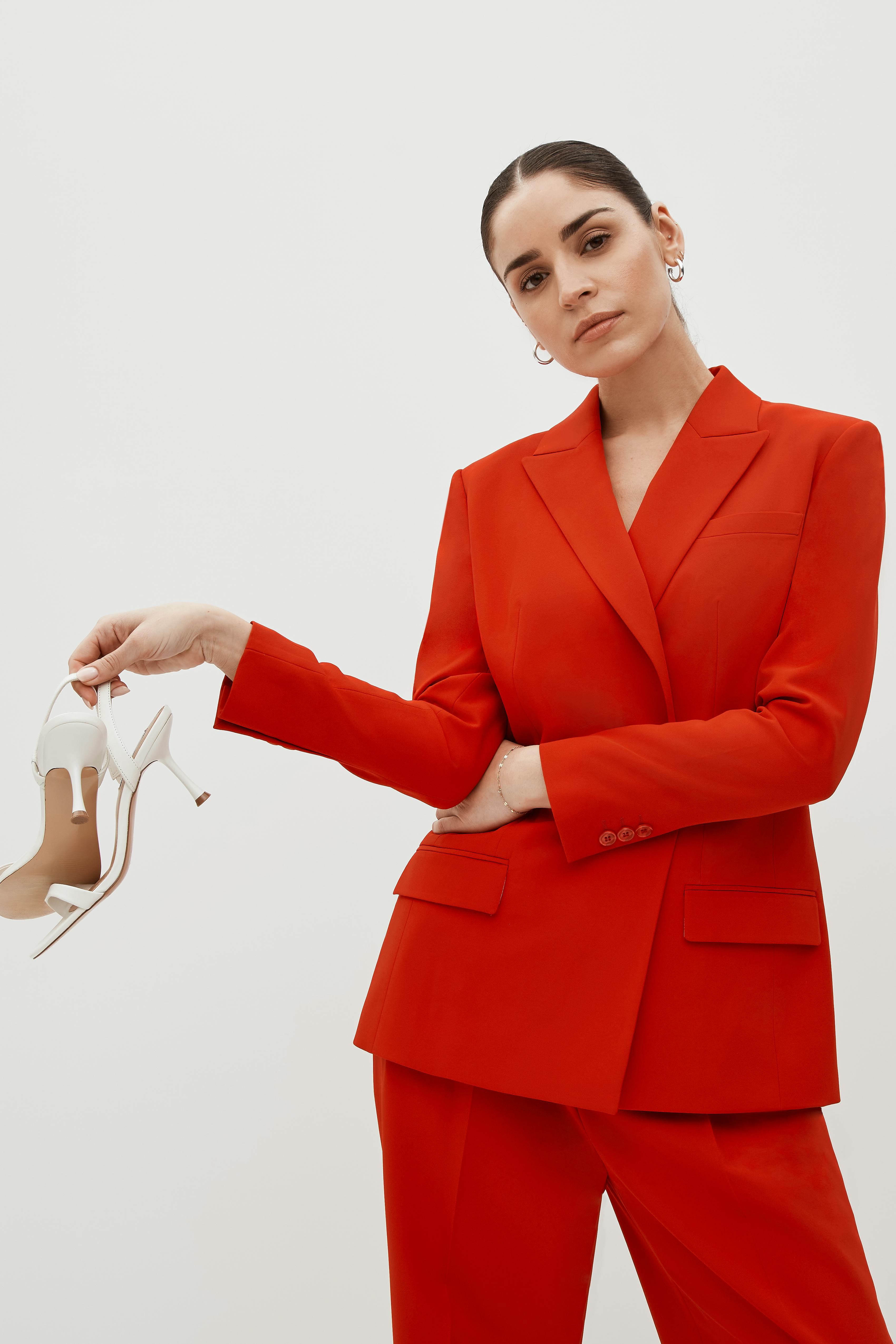 Women's holiday party style in bright red drapey pant suit with high heels.