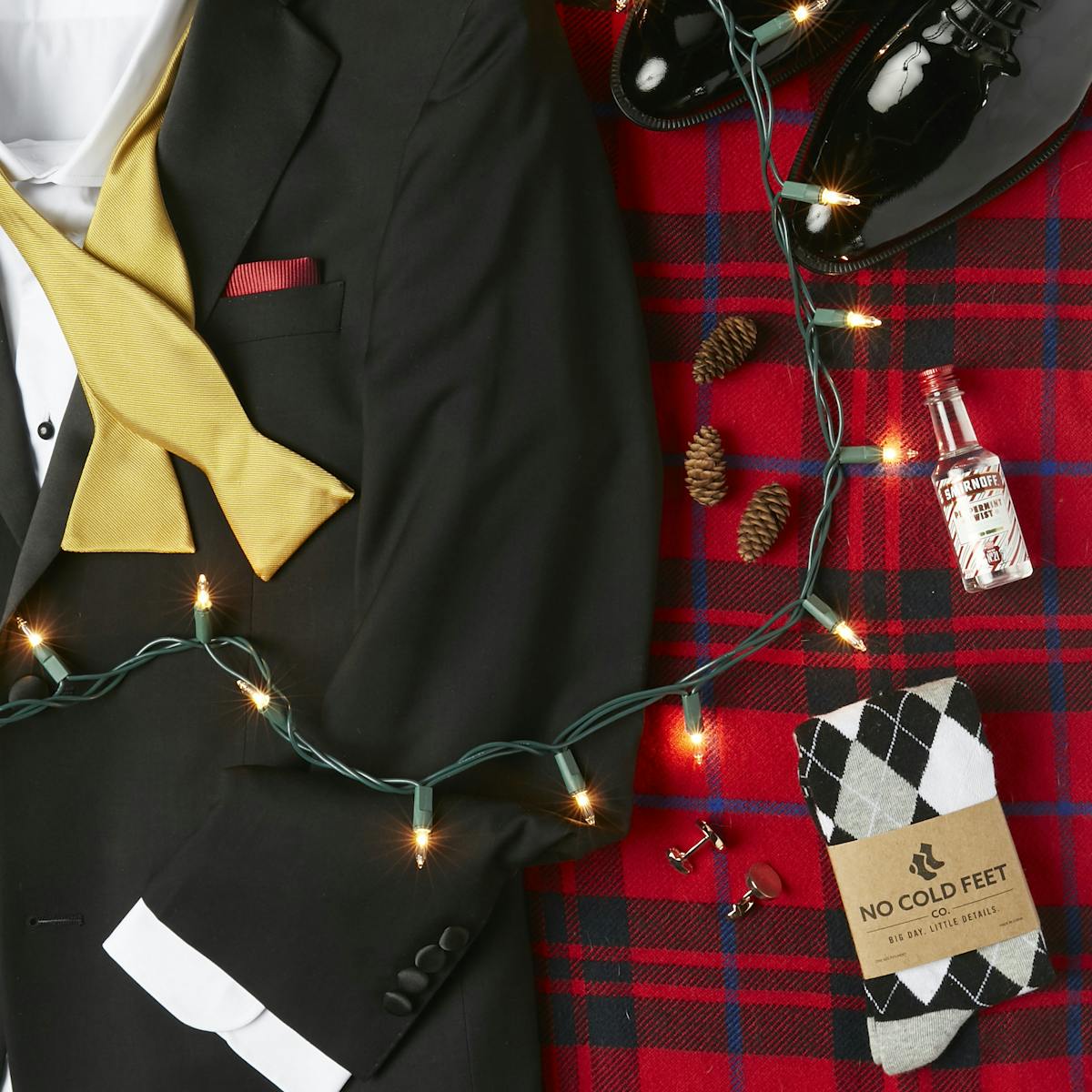 Festive flatlay featuring a black tuxedo, holiday patterns, and Christmas lights