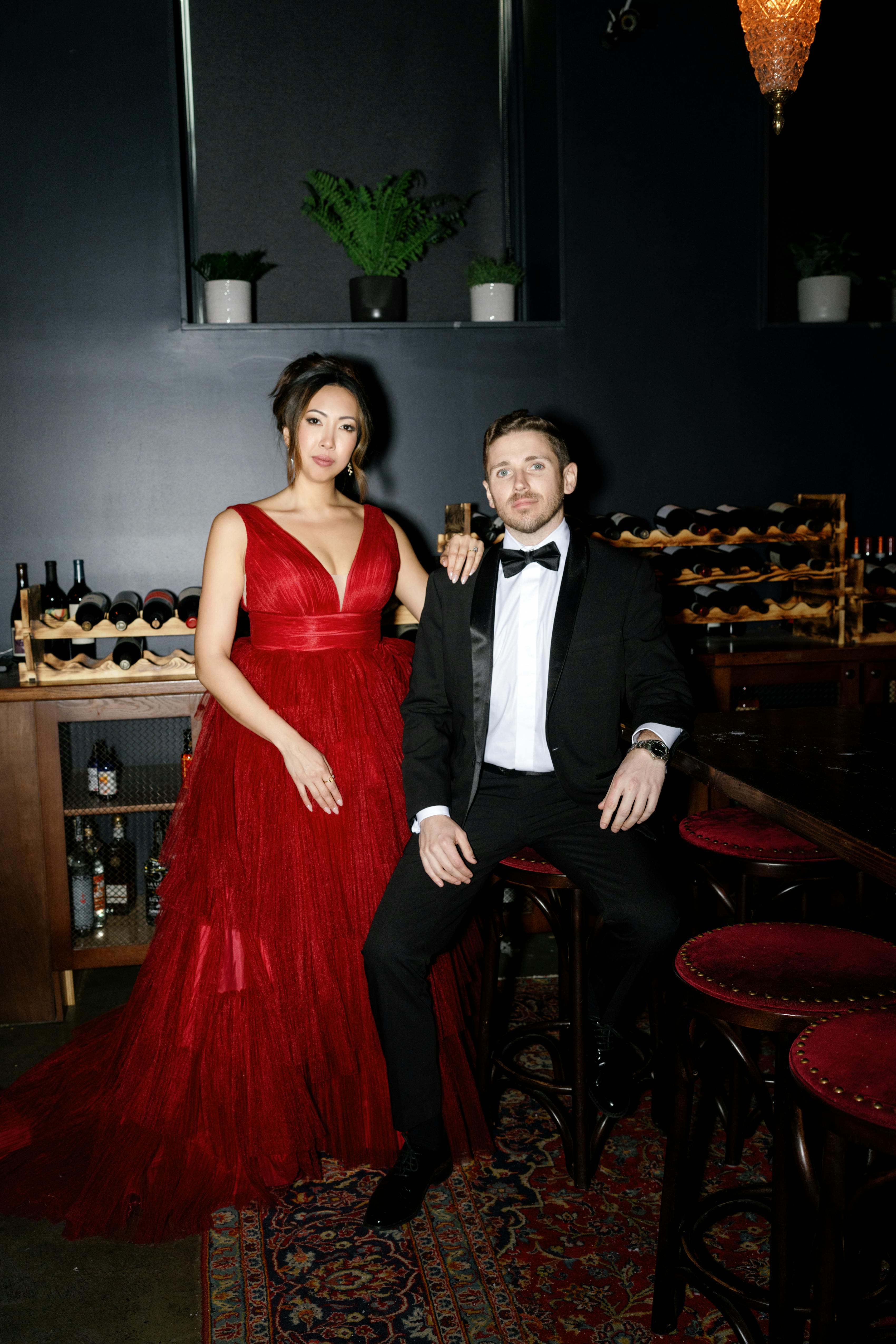Holiday party guests wearing a red floor length gown and a classic black tuxedo
