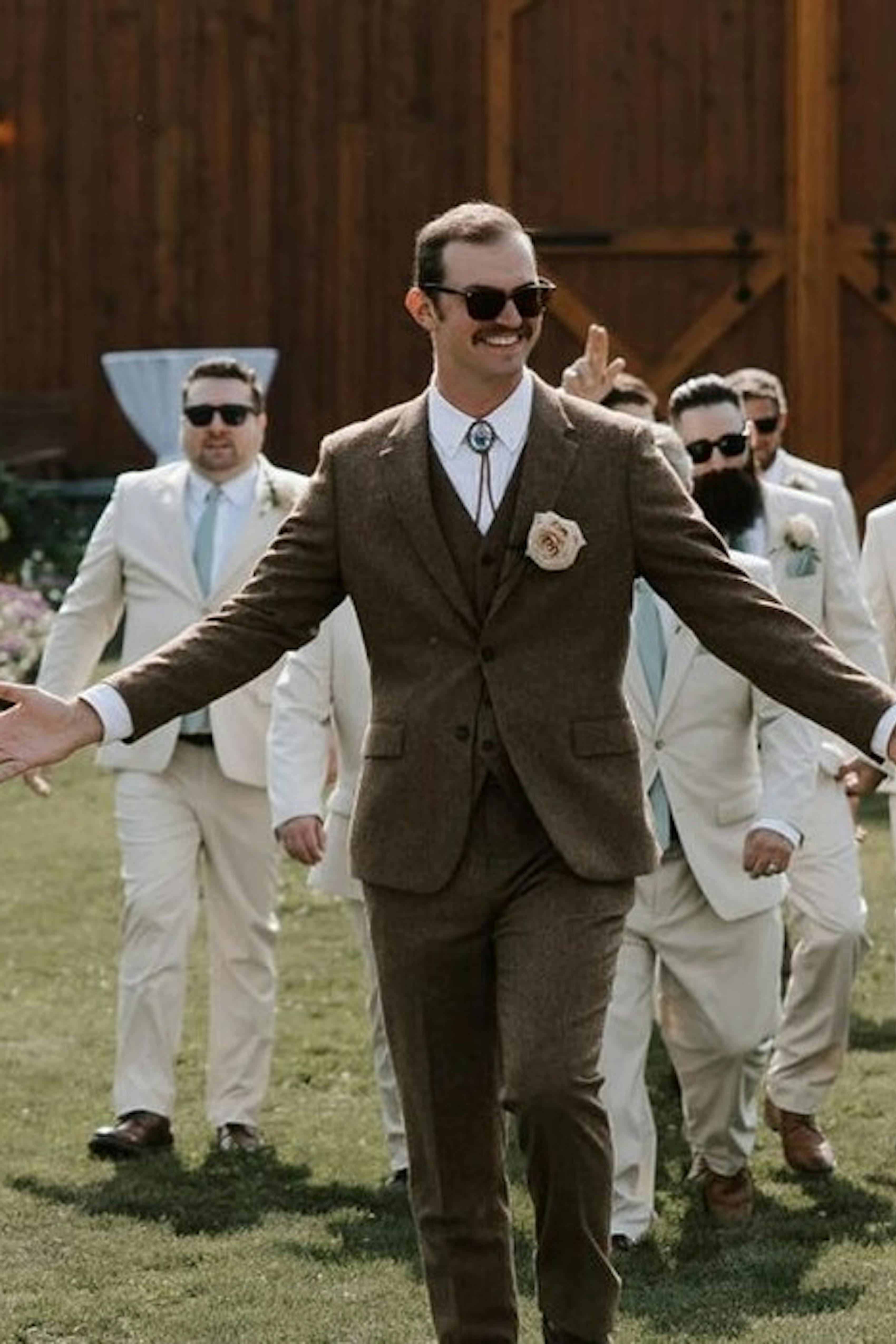 Brown tweed groom's suit paired with light tan groomsman suits for outdoor wedding