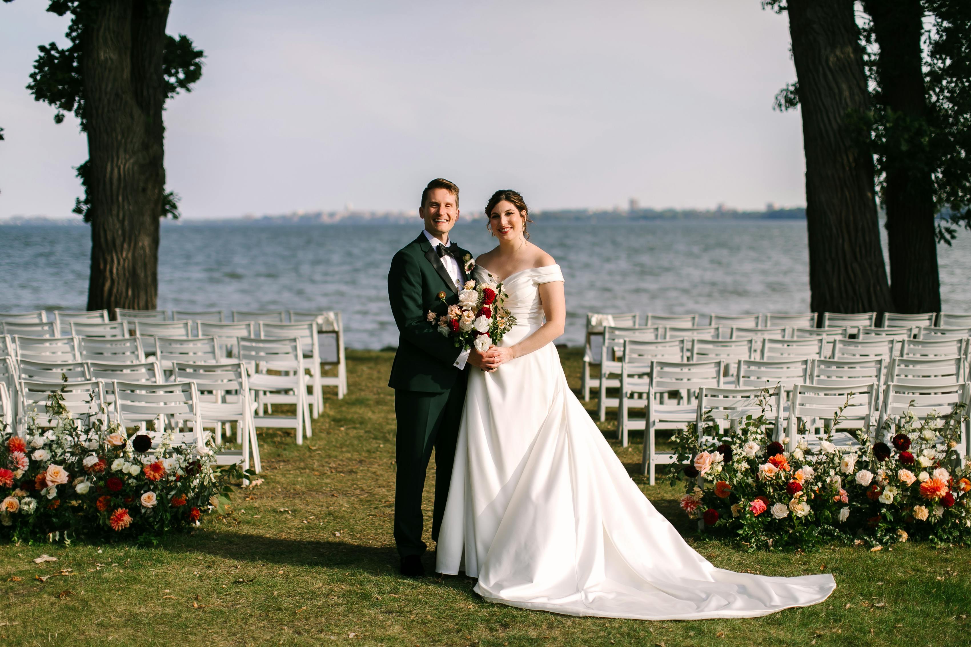 Bride and groom pose in front of their wedding ceremony set up in a lakefront location.