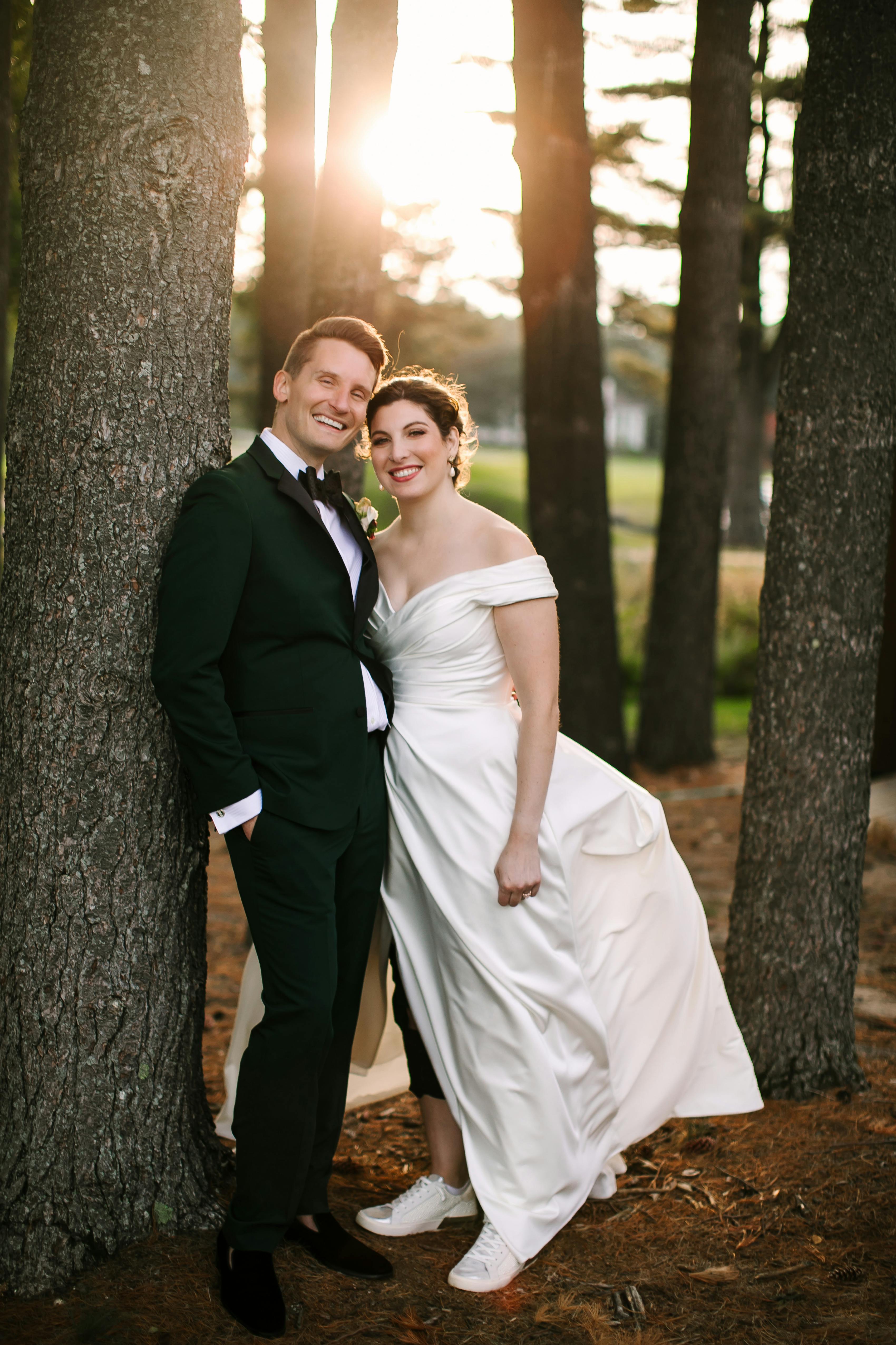 Bride and groom pose in a forest at sunset. The bride wears white sneakers to accompany her wedding dress.