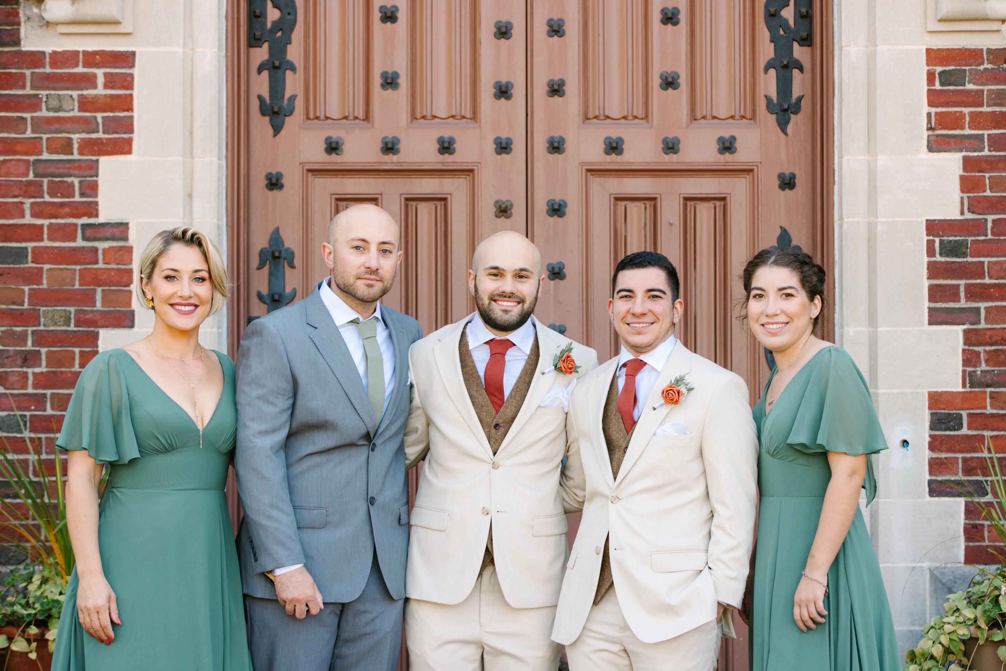 Two grooms in tan wedding suits & tweed suit vests, with bridal party in light grey and sage green