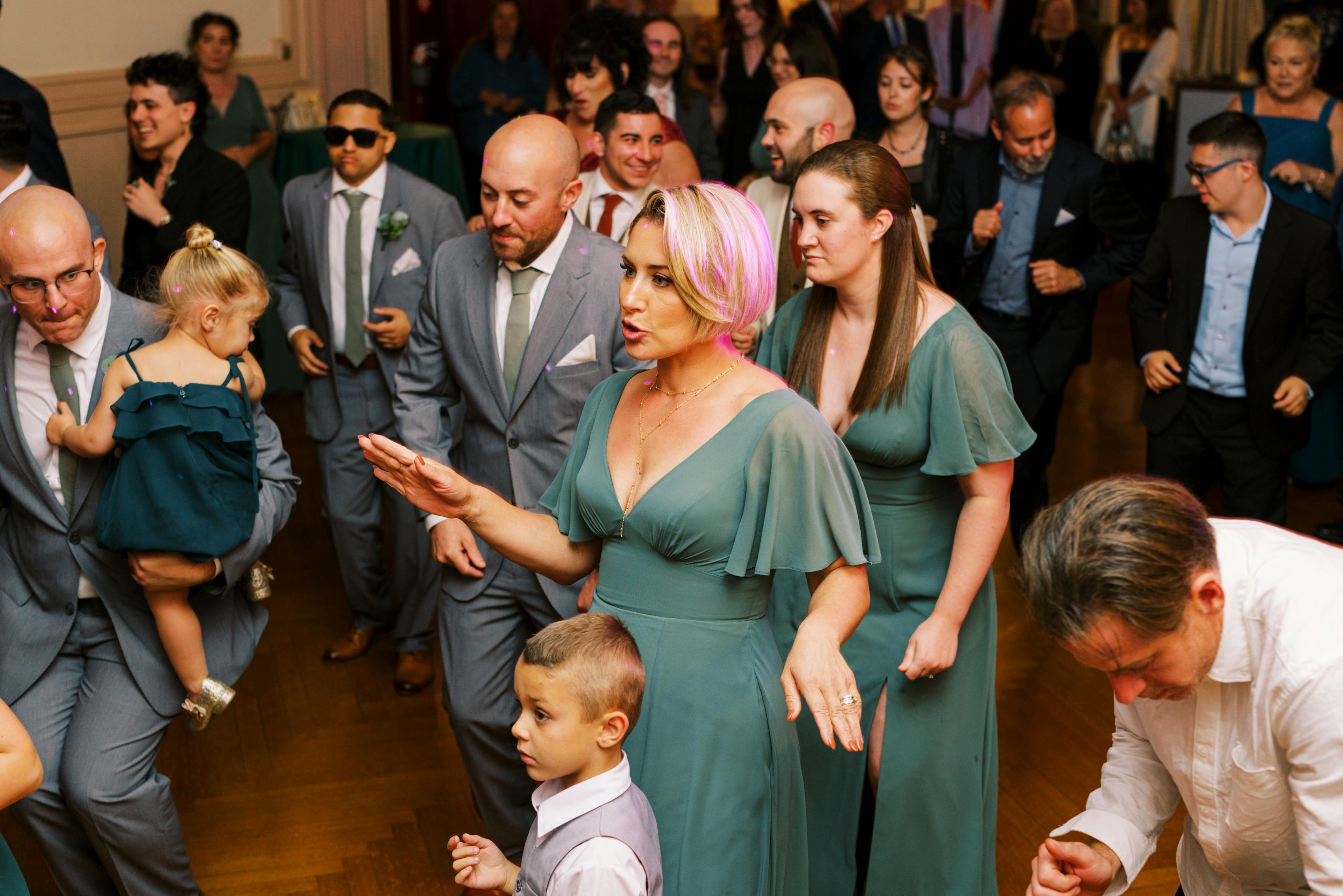 Wedding guests in light gray groomsmen suits & emerald or sage green bridesmaid dresses dancing