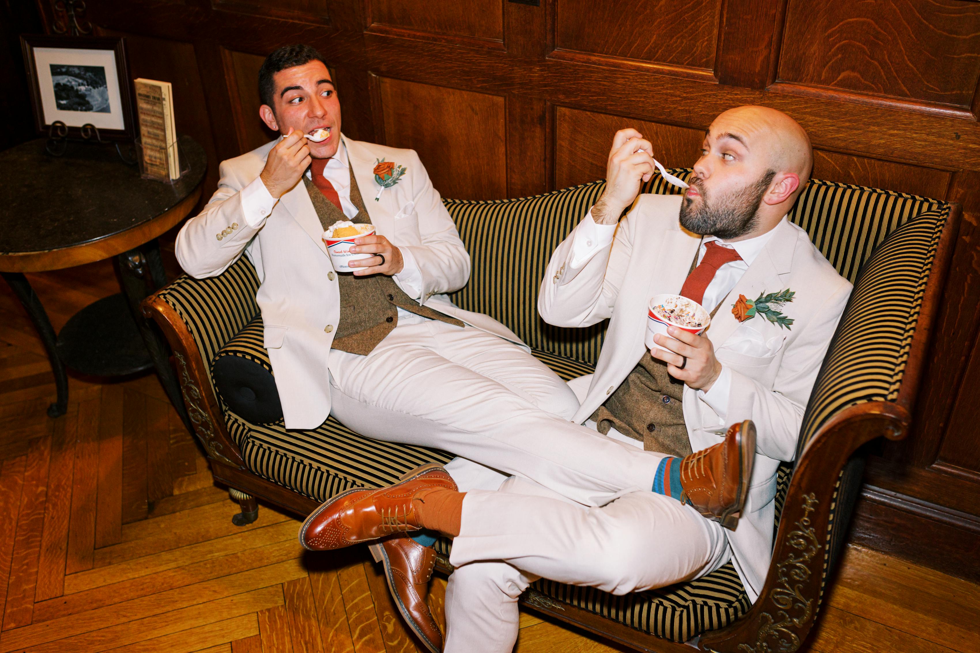 Grooms in tan wedding suits and tweed vests eating ice cream in vintage aesthetic venue