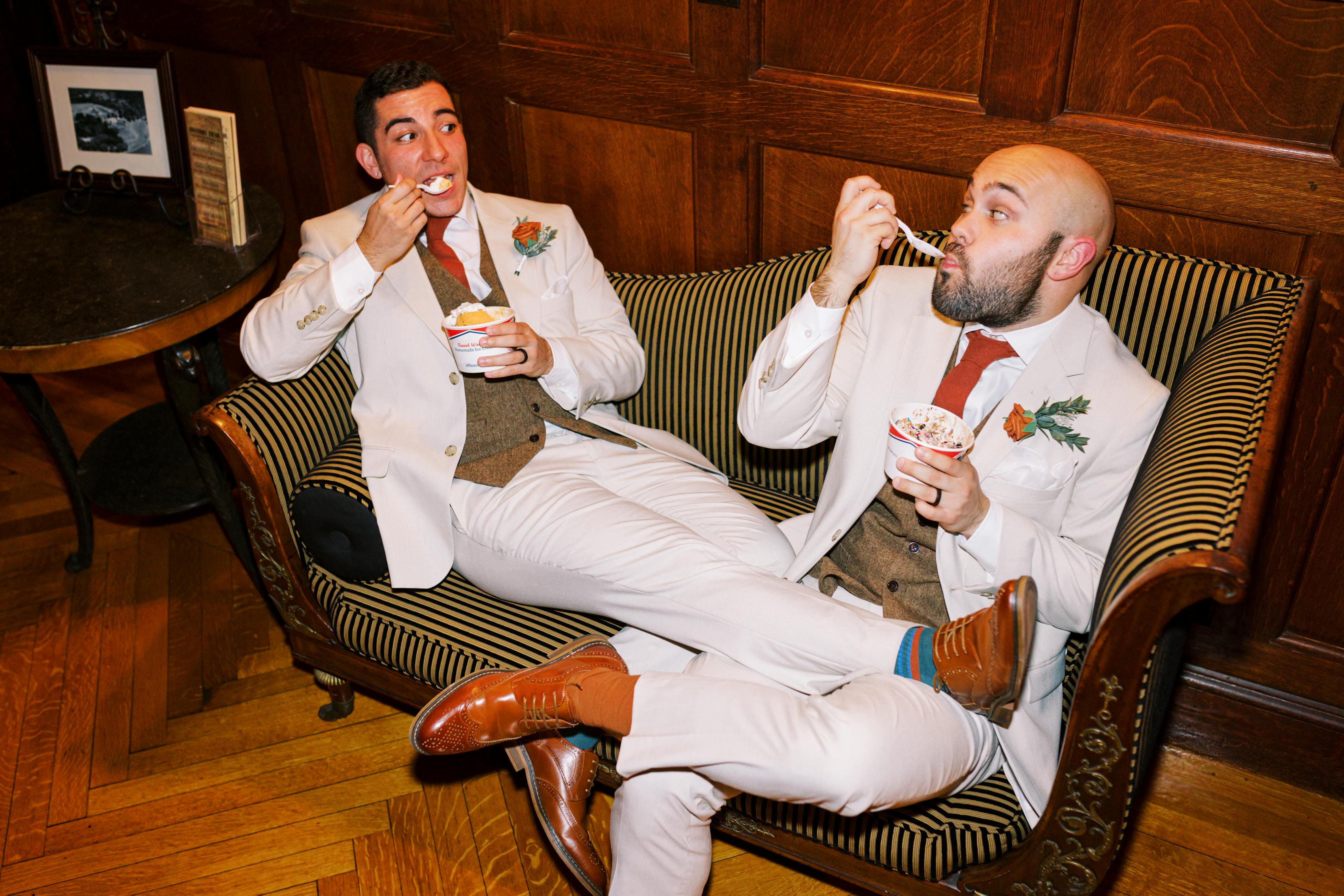 Grooms in tan wedding suits and tweed vests eating ice cream in vintage aesthetic venue