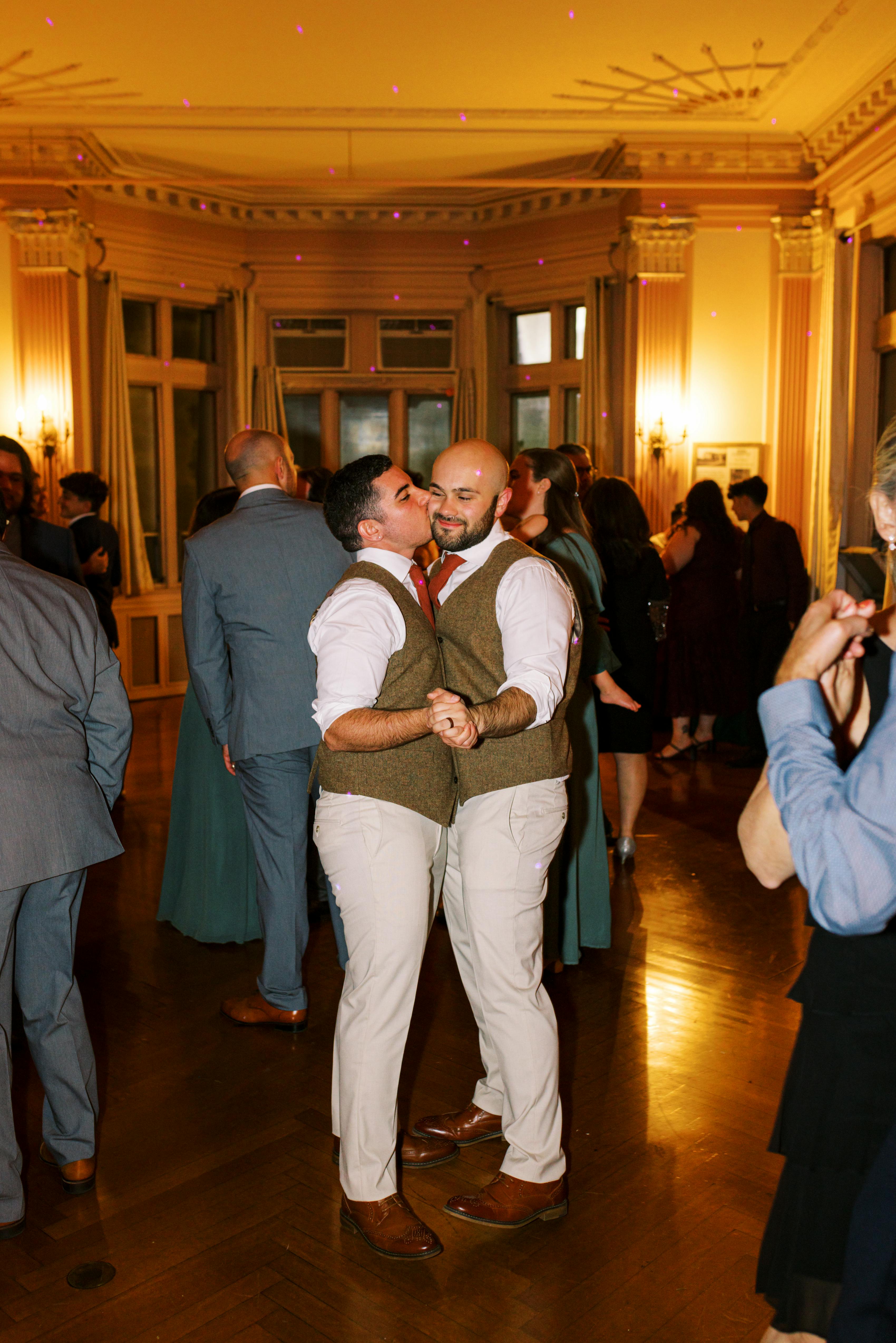 Two grooms dancing on the dance floor wearing matching tweed suit vests and tan suit pants