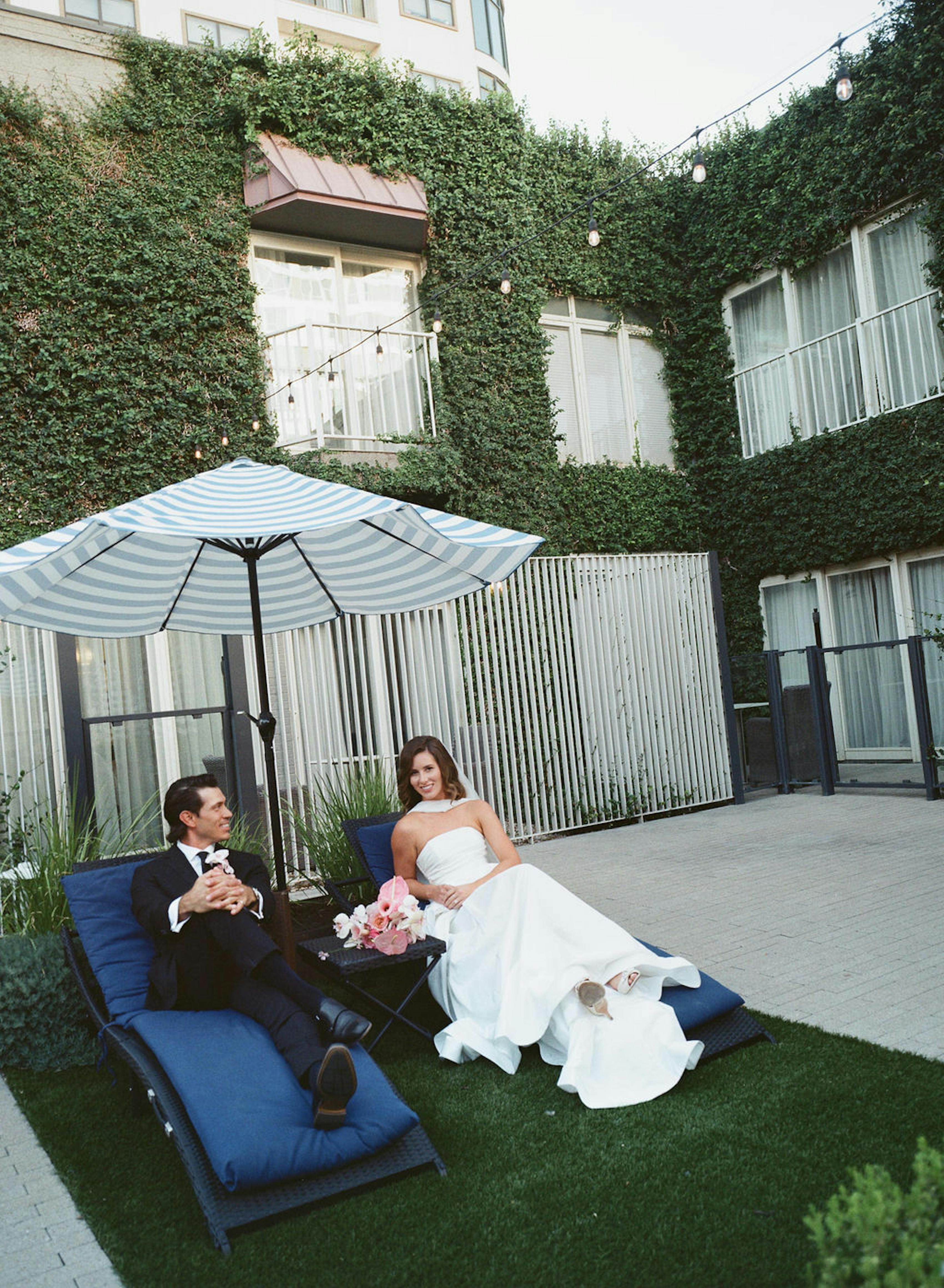 Poolside wedding attire with black tuxedo groom and wedding dress with scarf bride
