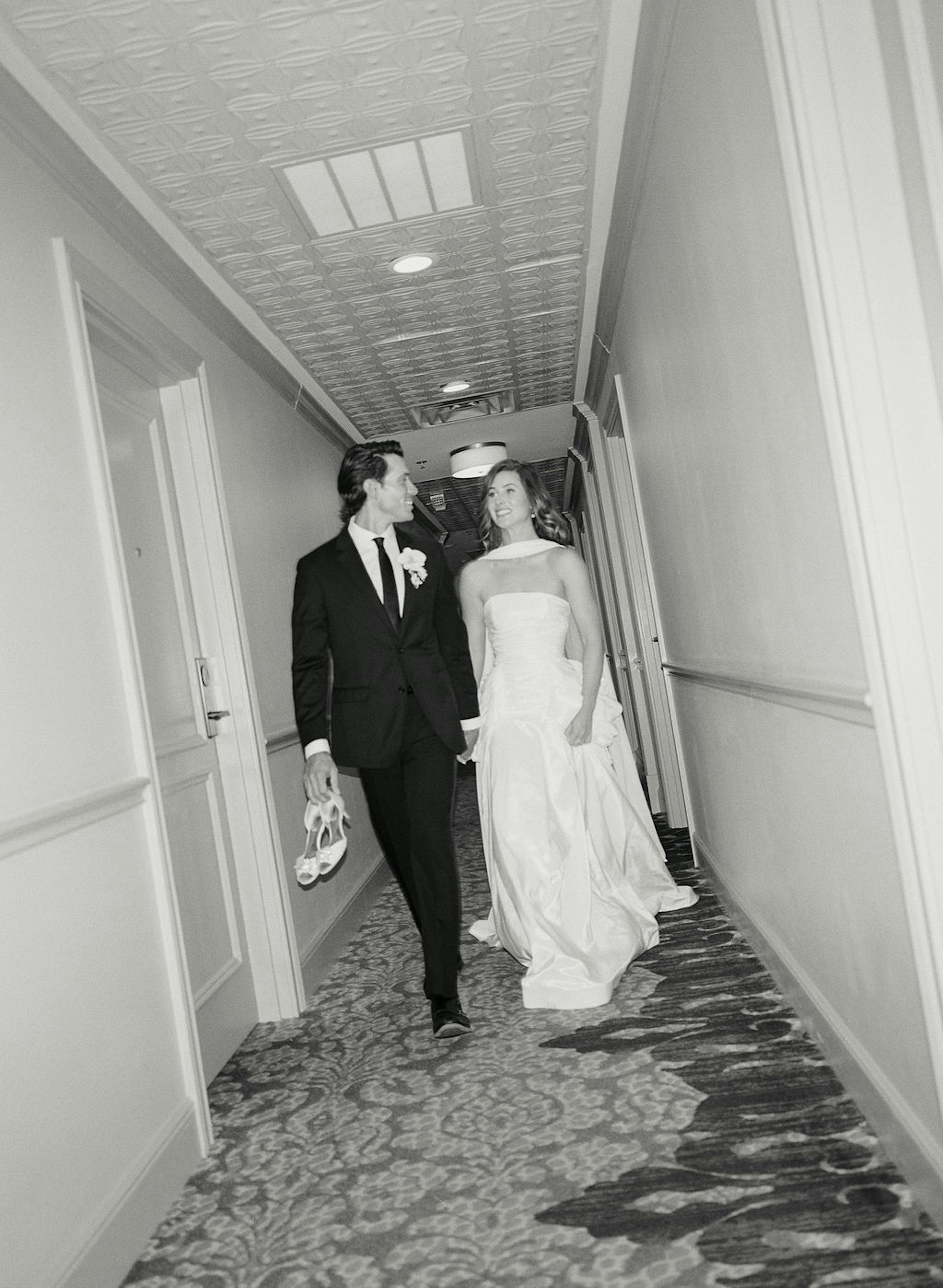Bride and groom stroll the hallway of their hotel after the wedding reception.