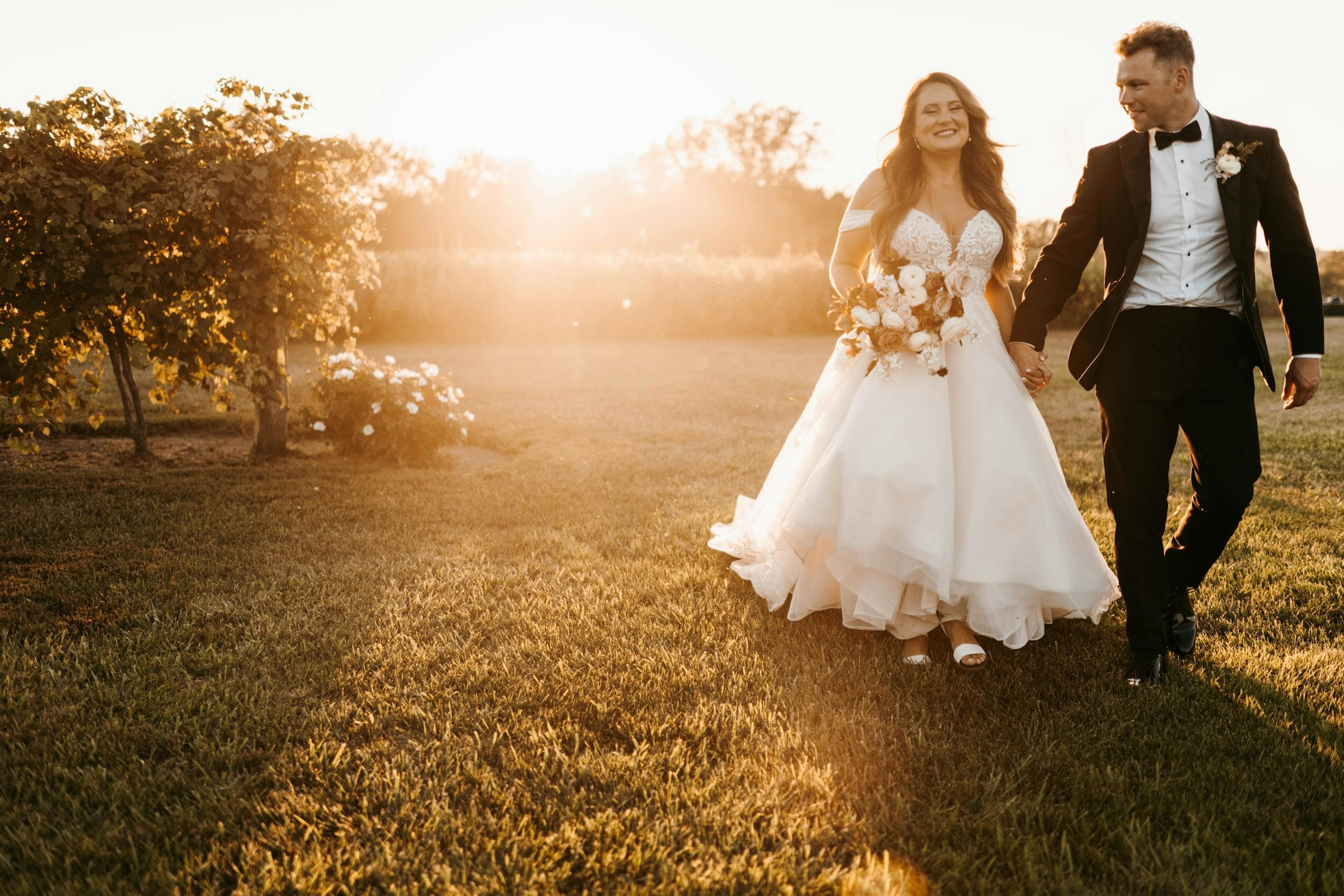 bride and groom in black tie walk through a vineyard at sunset