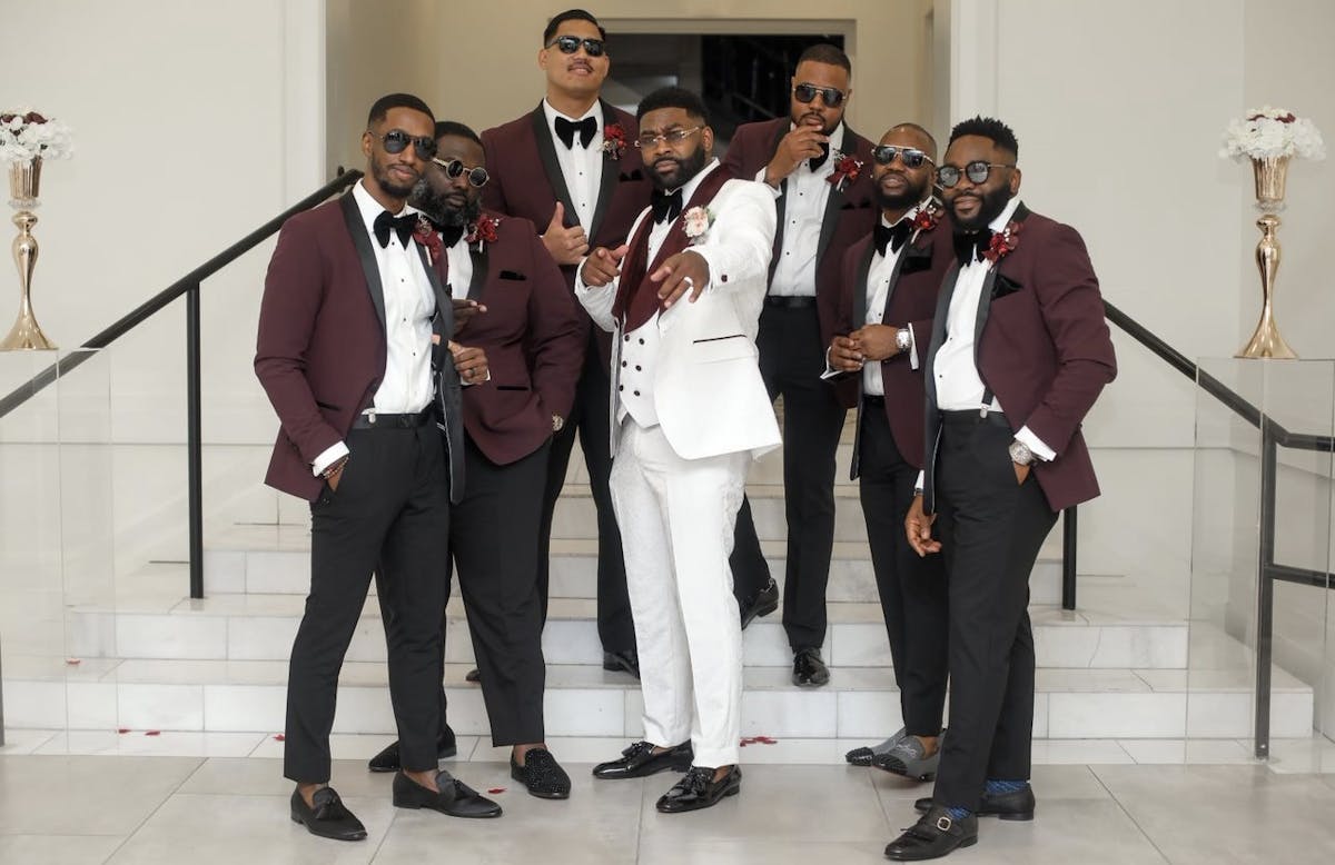 Groomsmen wearing burgundy tuxedos posing with groom wearing ivory tuxedo with burgundy lapel