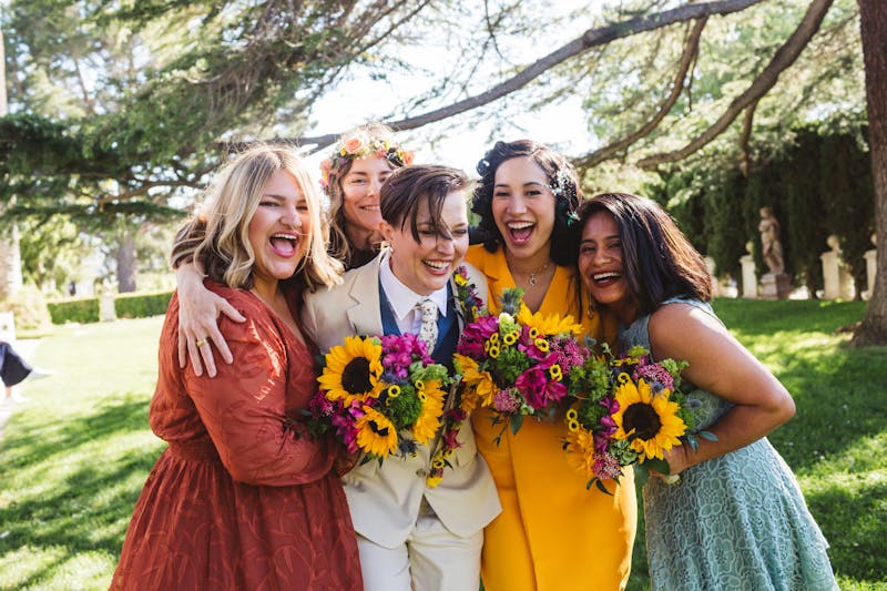 Bright colorful spring bridal party hug with sunflower bouquets in tan, yellow, and pink wedding color palette.