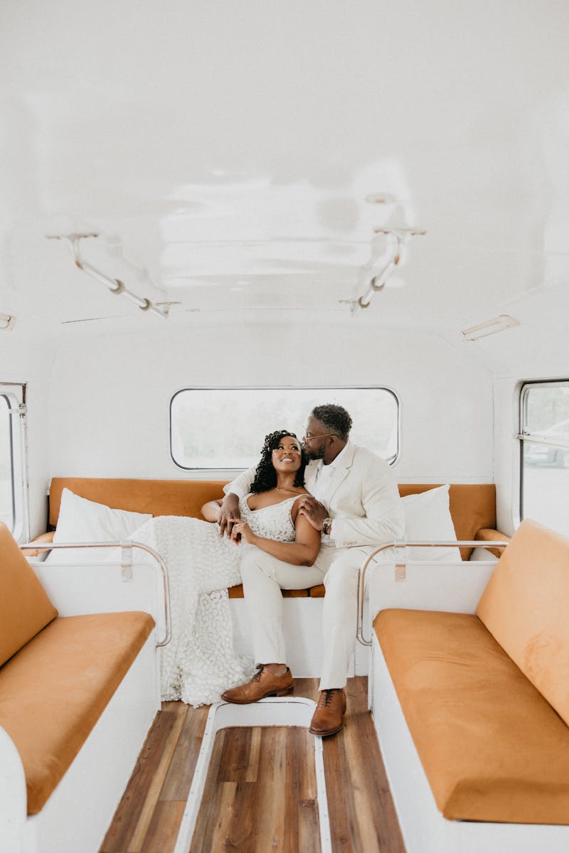 Neutral color palette bride and groom in white wedding gown and tan wedding suit lounging inside converted bus venue