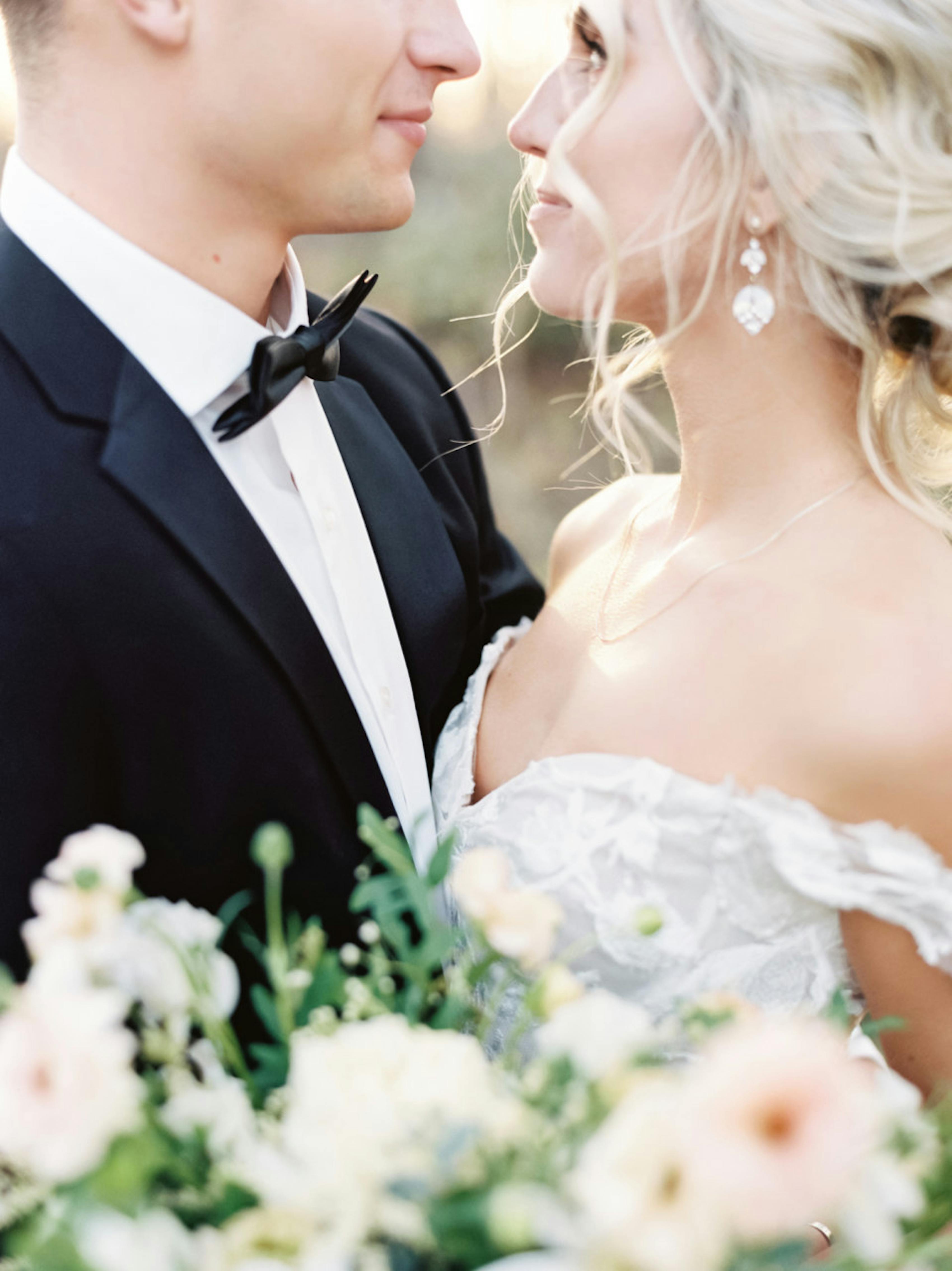 Close up details groom's black tuxedo jacket while he holds bride for creative wedding portrait.