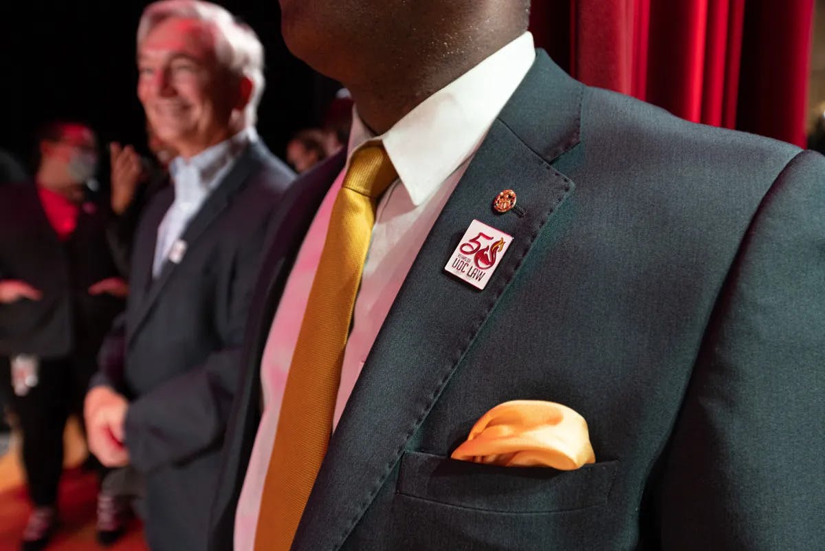 Student wearing special 50th anniversary design pin on grey suit jacket for law school ceremony.
