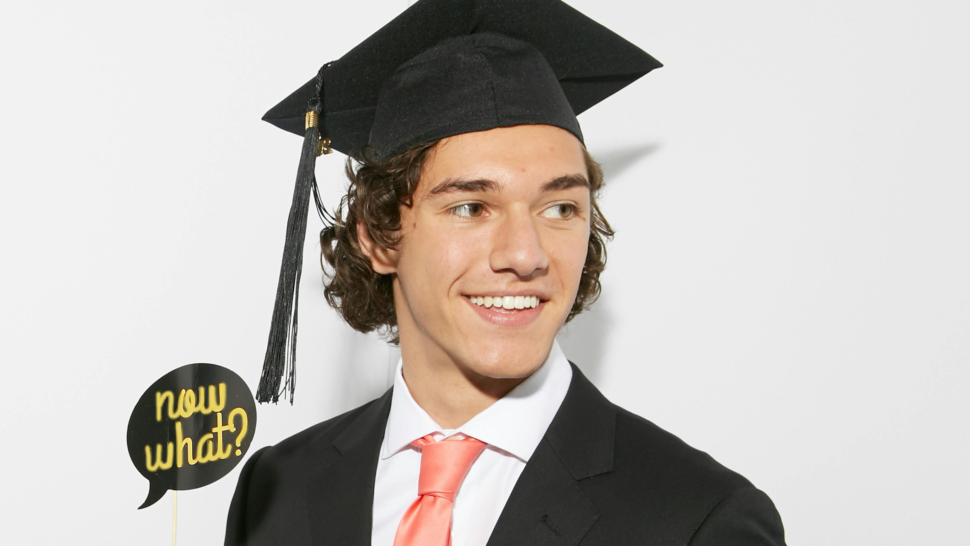 Graduate wearing outfit with for cap and gown holding "now what" sign for grad photos