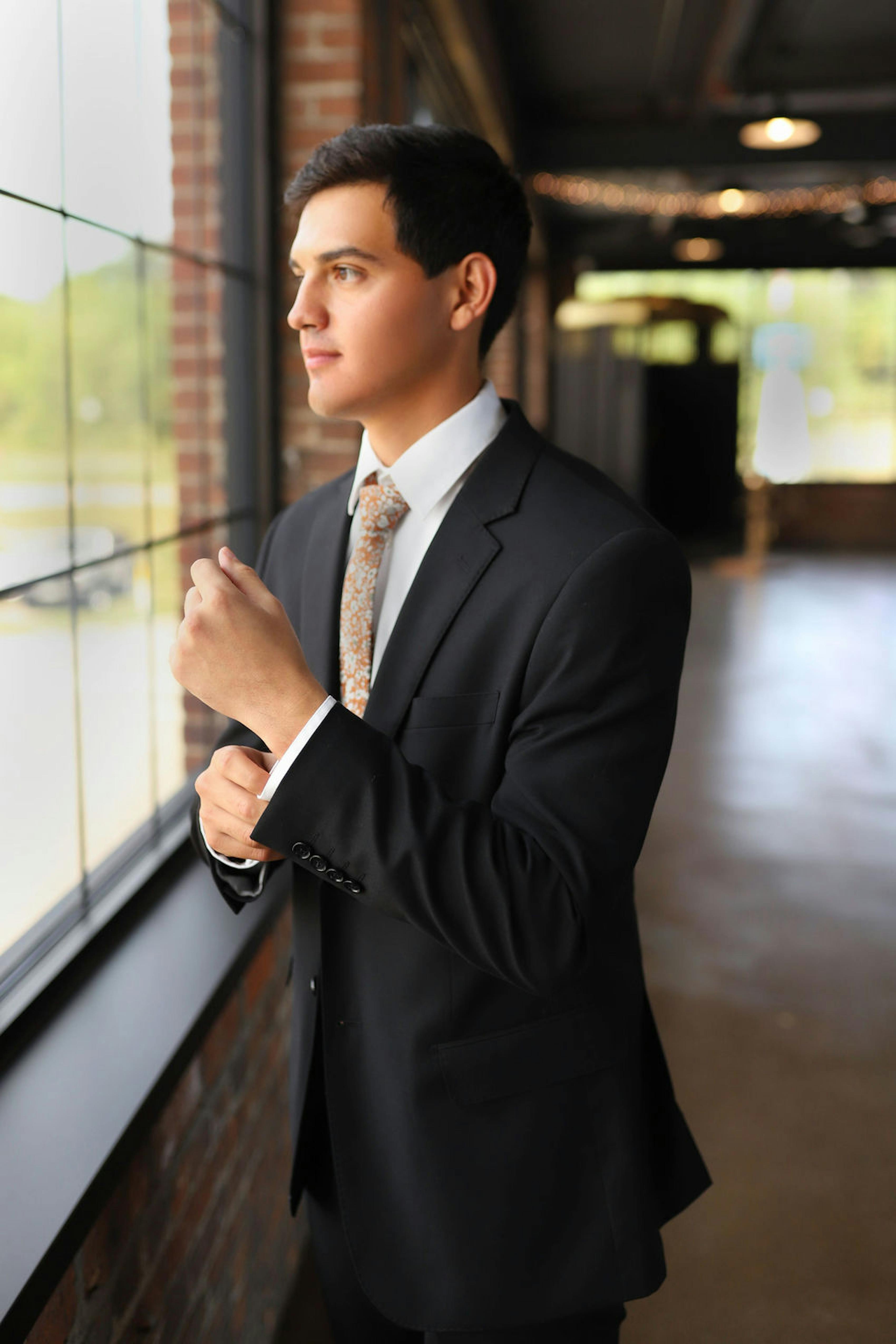 Man wearing black suit graduation outfit with orange floral tie for school colors