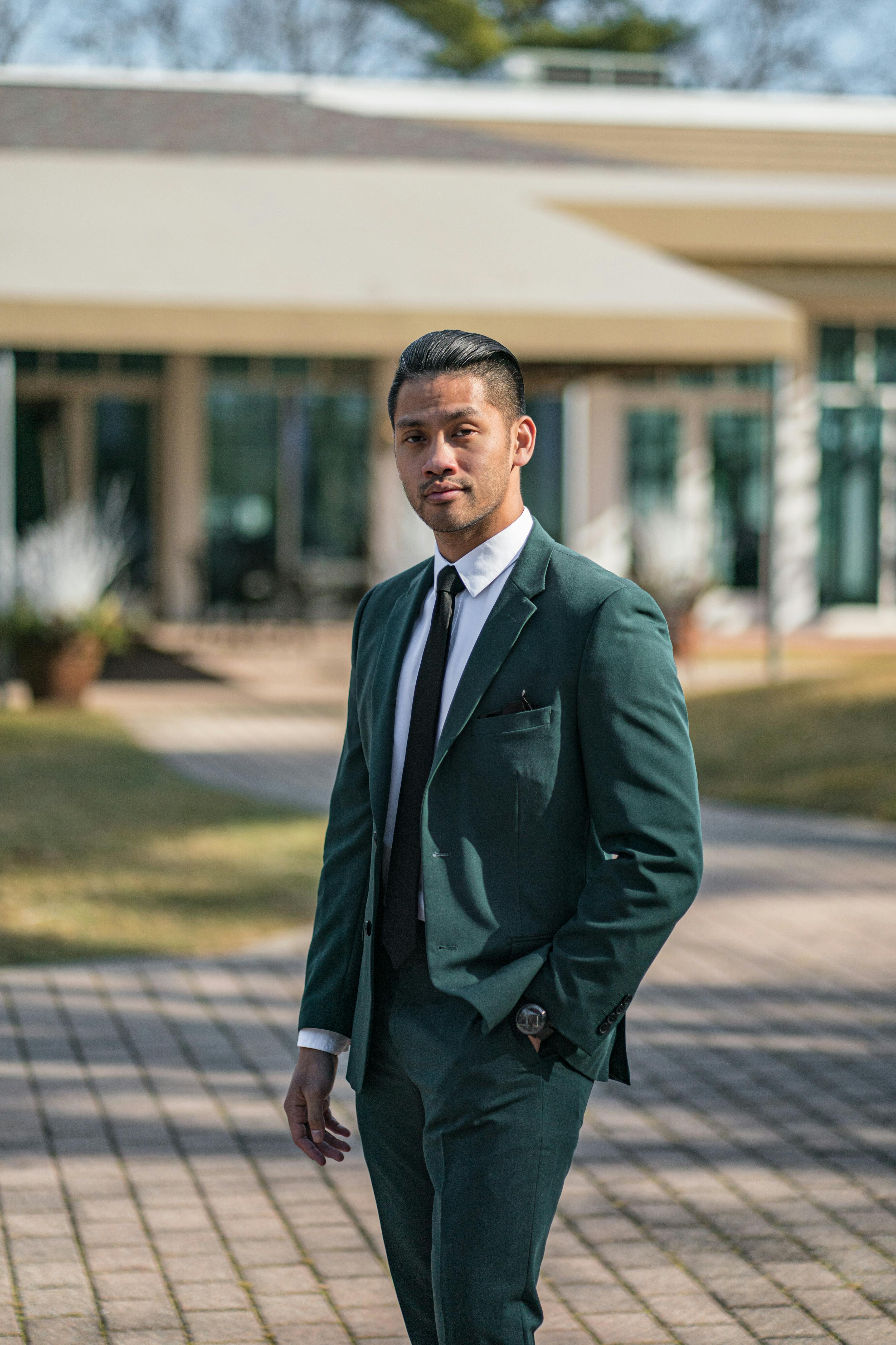 Man wearing dark green suit for outdoor graduation standing in front of school