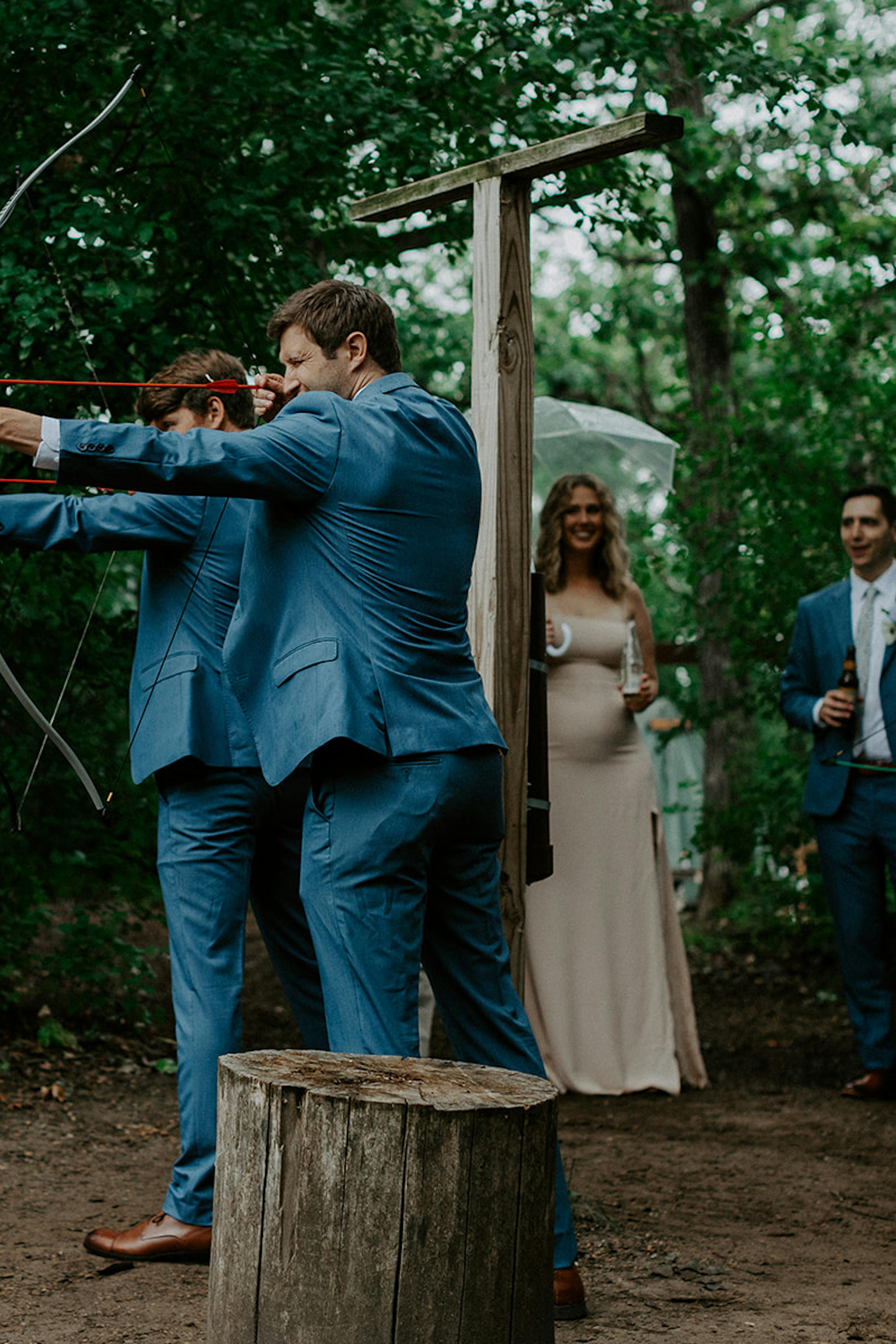 Groomsmen wearing light blue suits doing archery for camping wedding theme