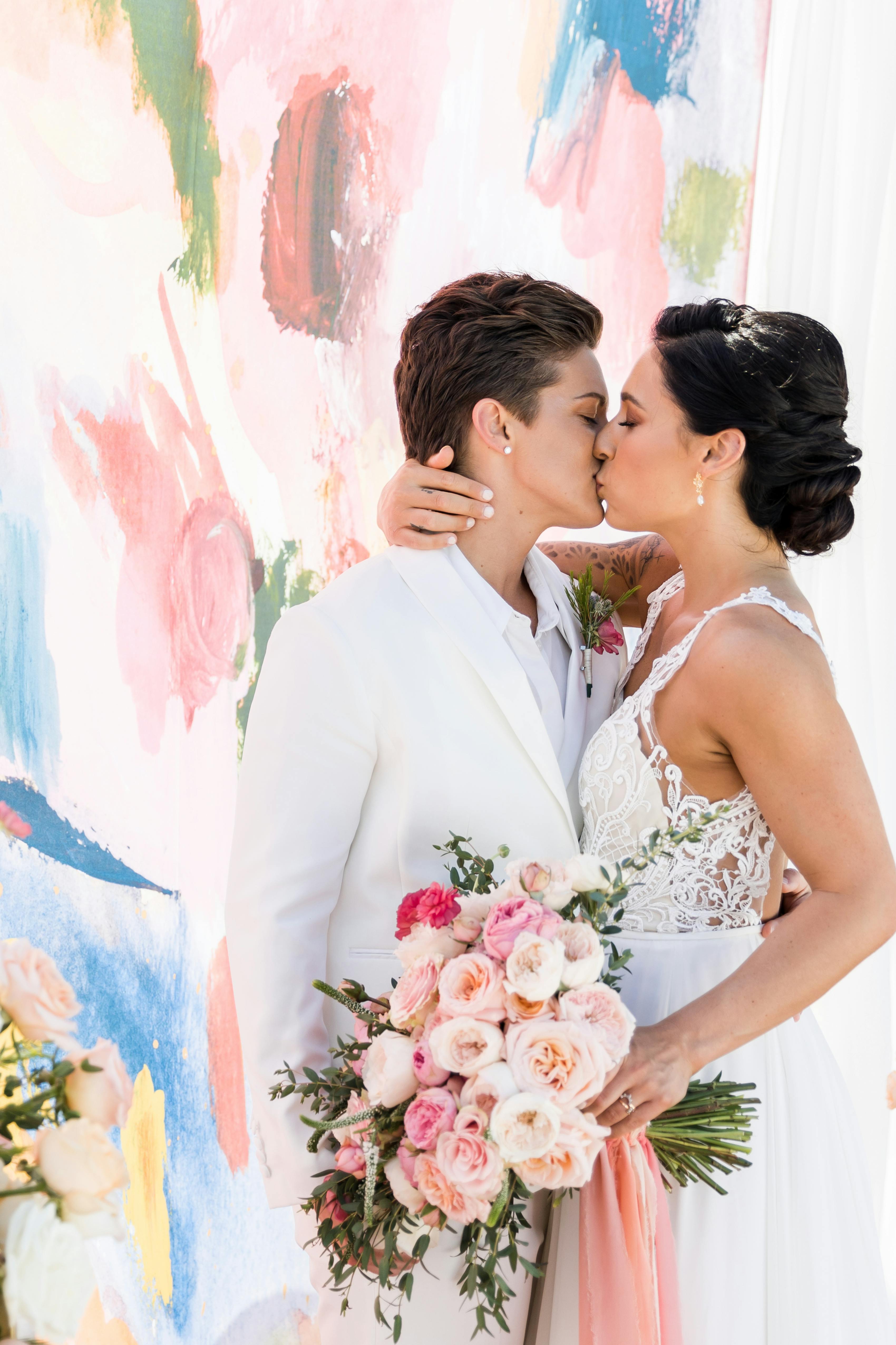 Pink and blue wedding backdrop for two brides wearing a white tuxedo and dress