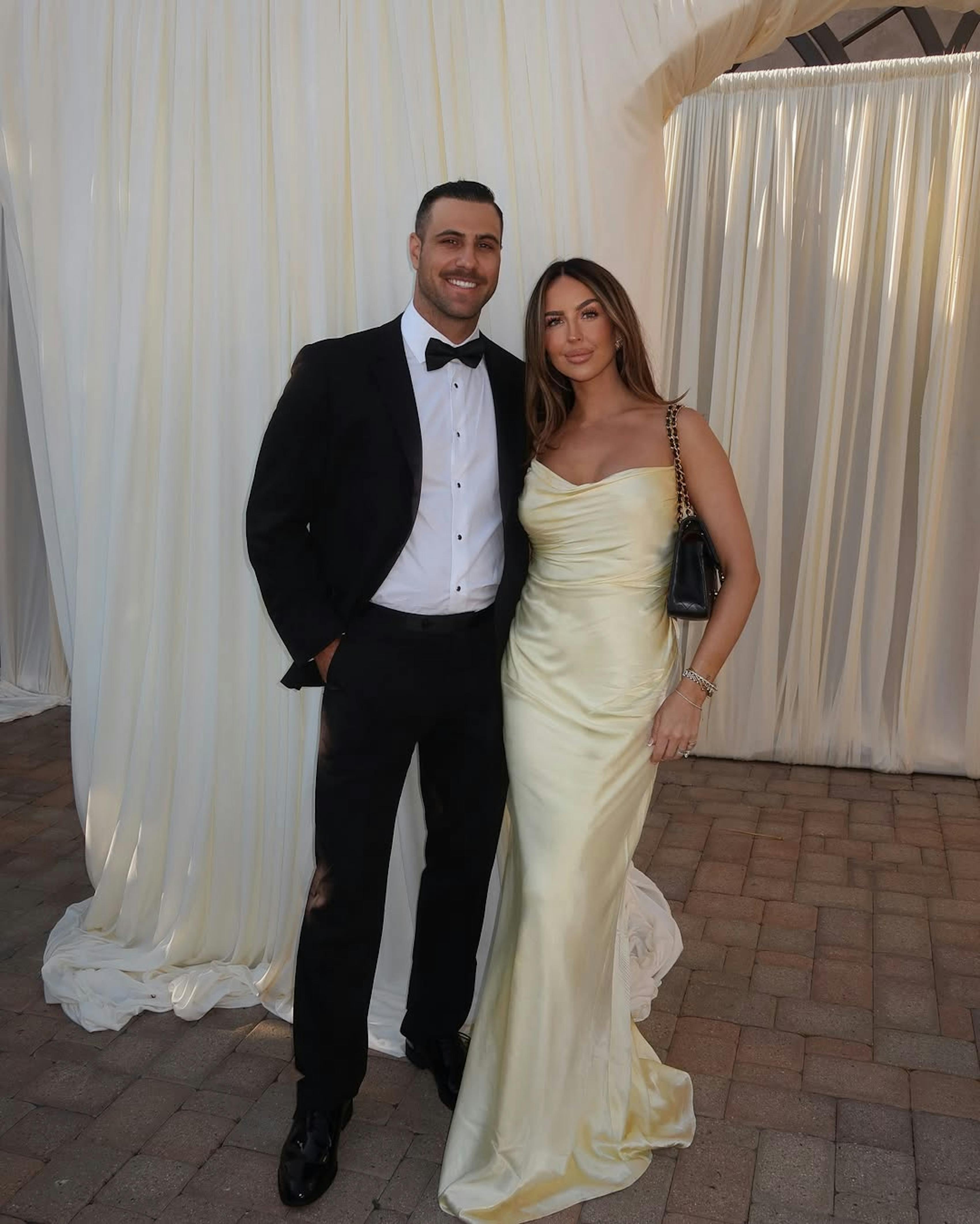 Black tie wedding guest outfits for couples in classic tuxedo and butter yellow gown