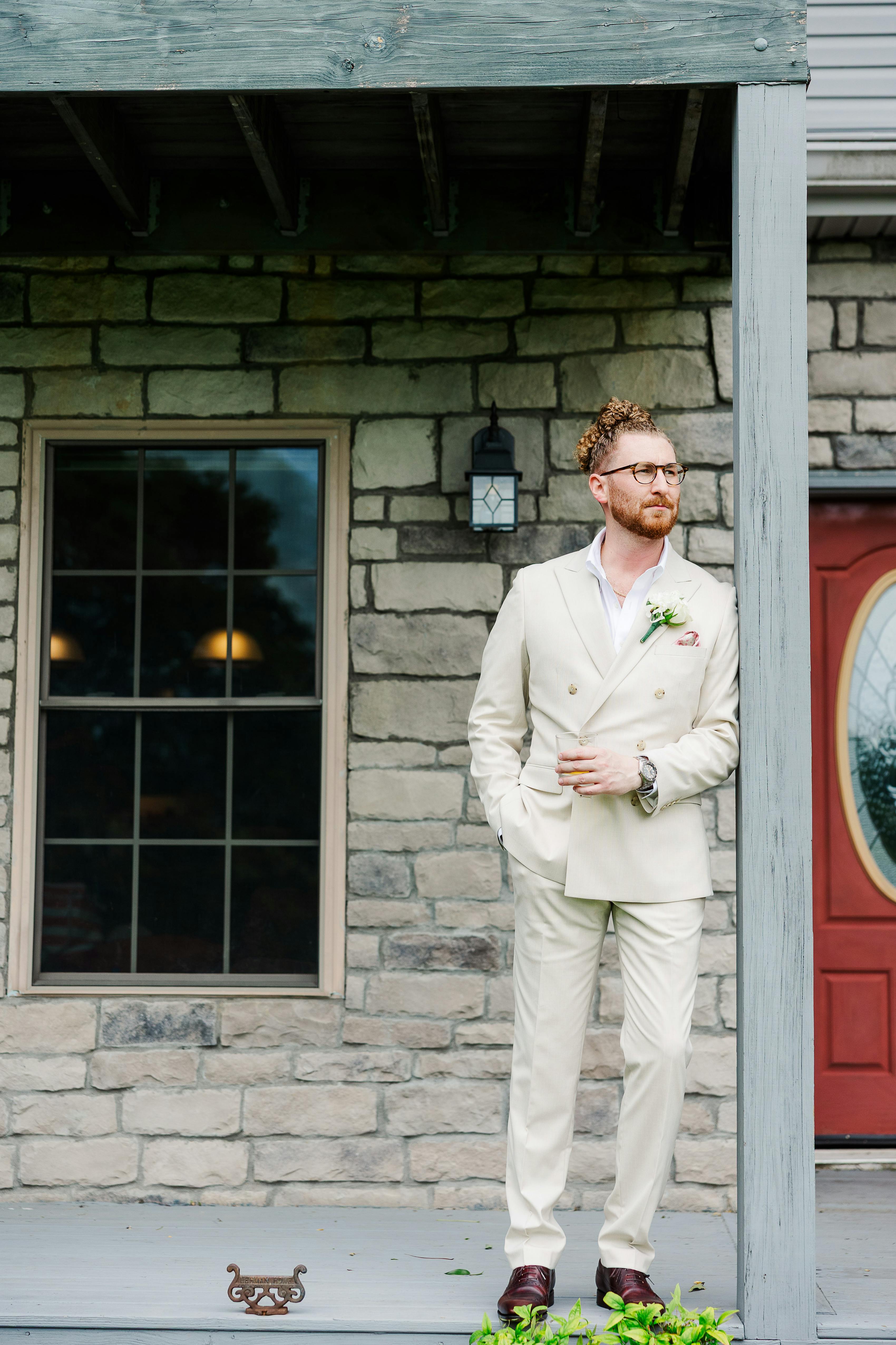 Groom wearing light tan double breasted suit outside for autumn wedding