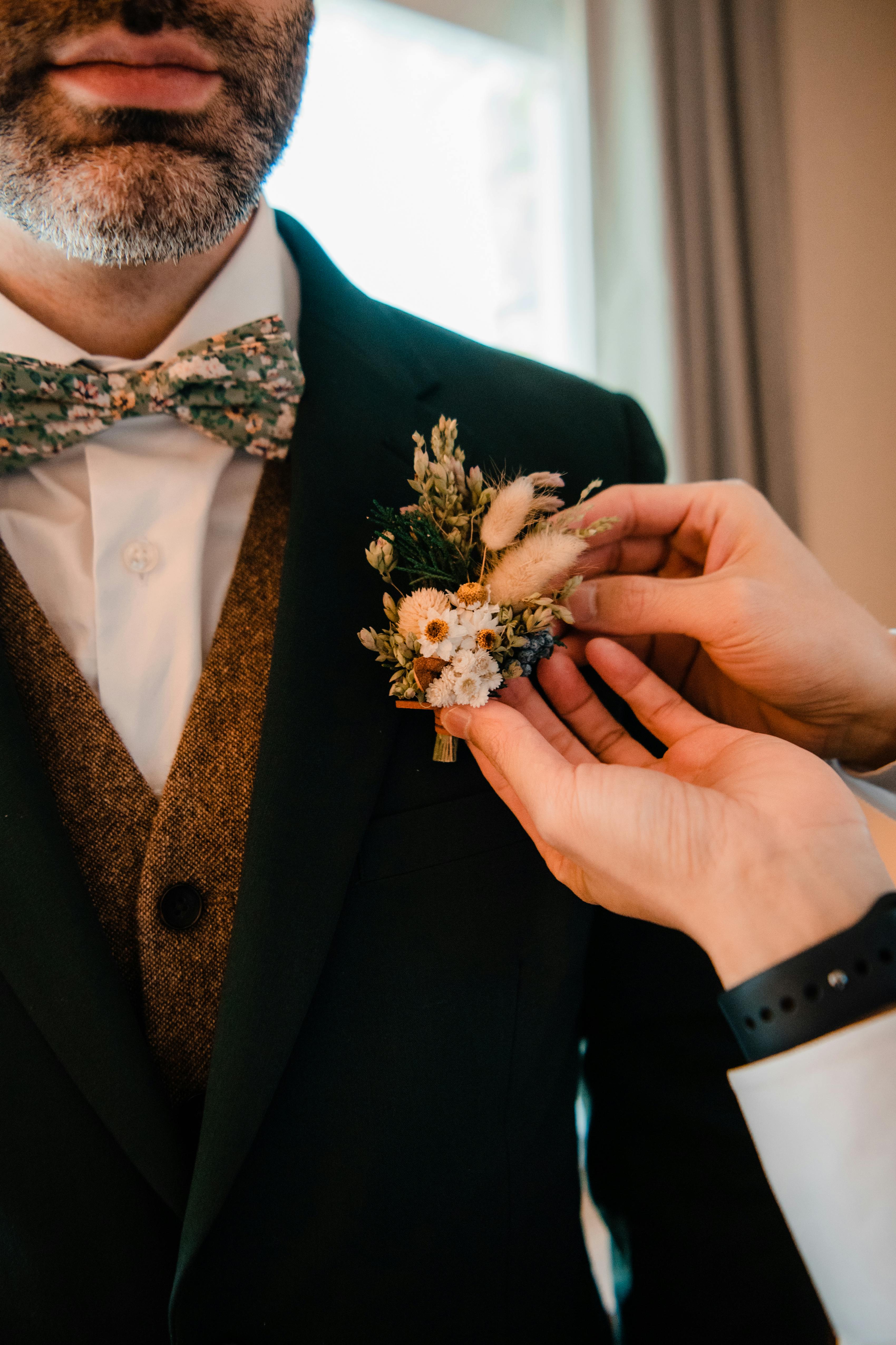 Groom's outfit with dark green suit, brown tweed waistcoat, and floral bow tie