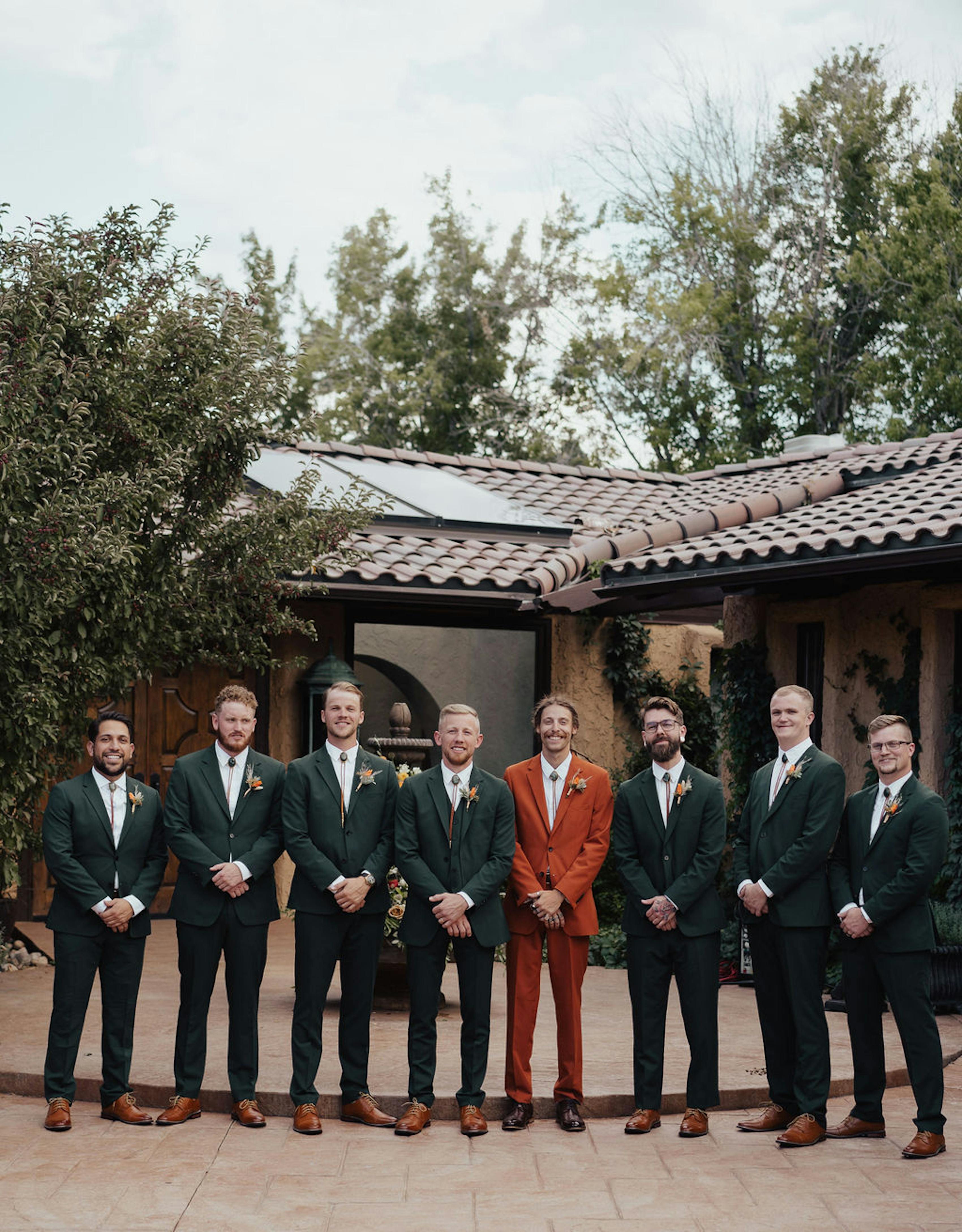Dark green groomsmen suits with a burnt orange suit for the groom
