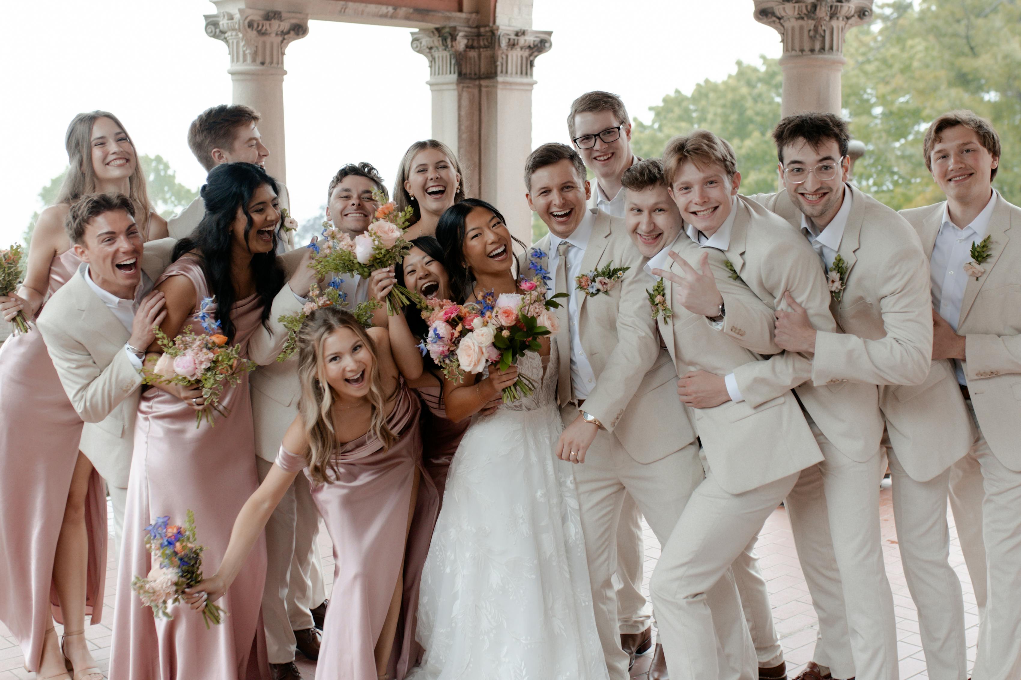 Tan groomsman suits with pink ties coordinating with satin bridesmaid dresses