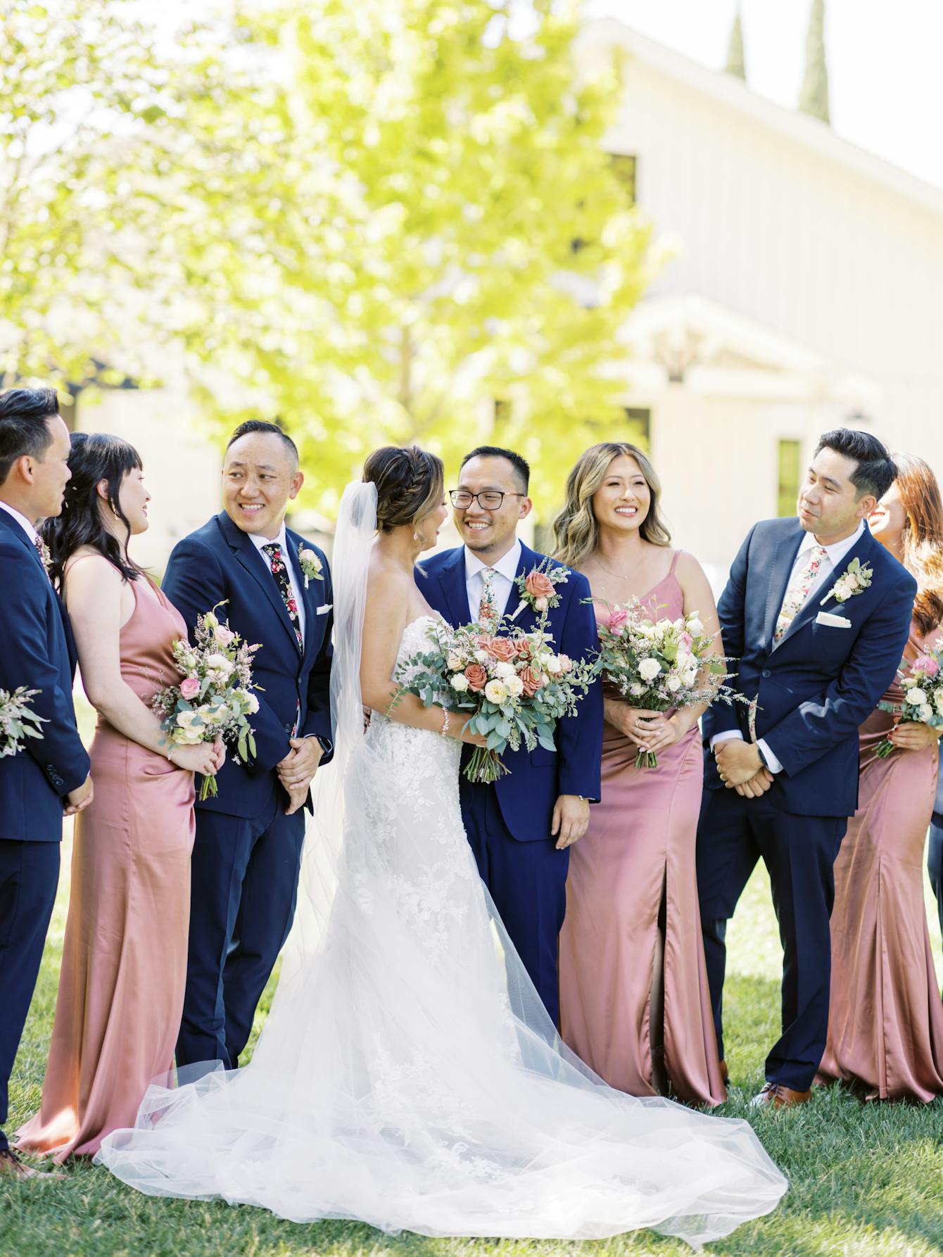 Wedding couple standing in the center of groomsmen in Navy Blue suits and bridesmaids in plum pink dresses.