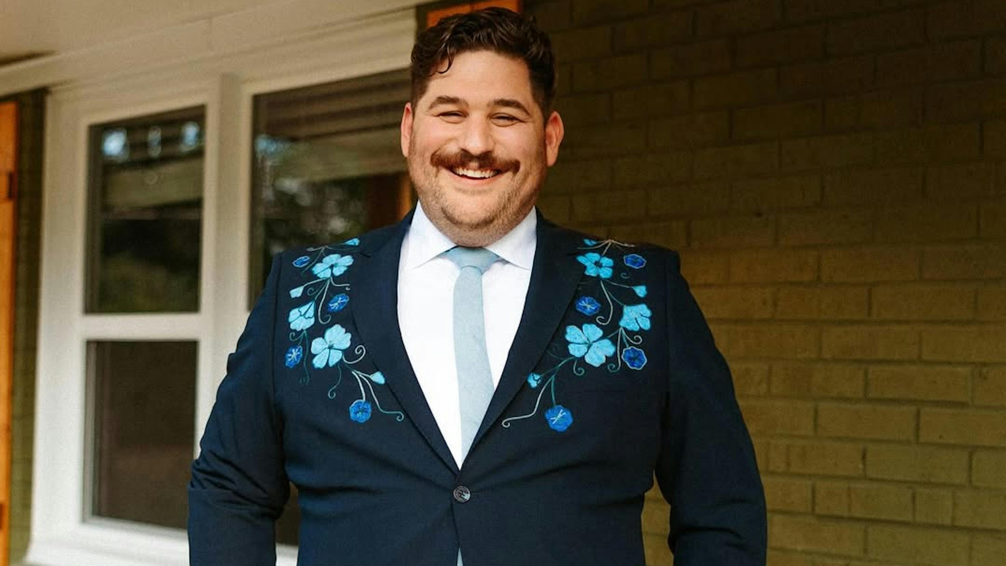 Smiling in men's navy suit embroidered with floral details