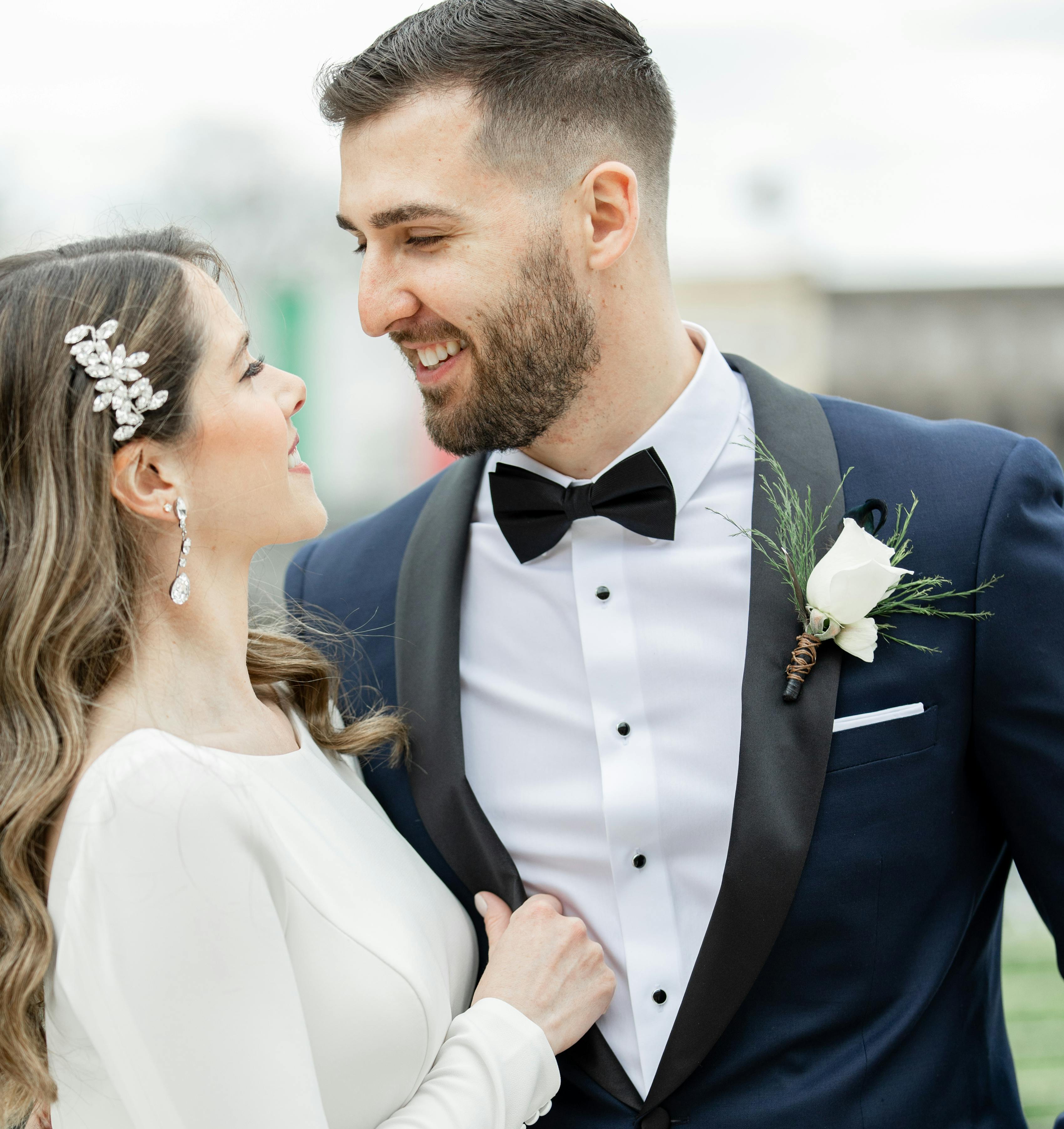 Groom wearing navy blue tuxedo with shawl lapel outdoors at winter wedding with bride